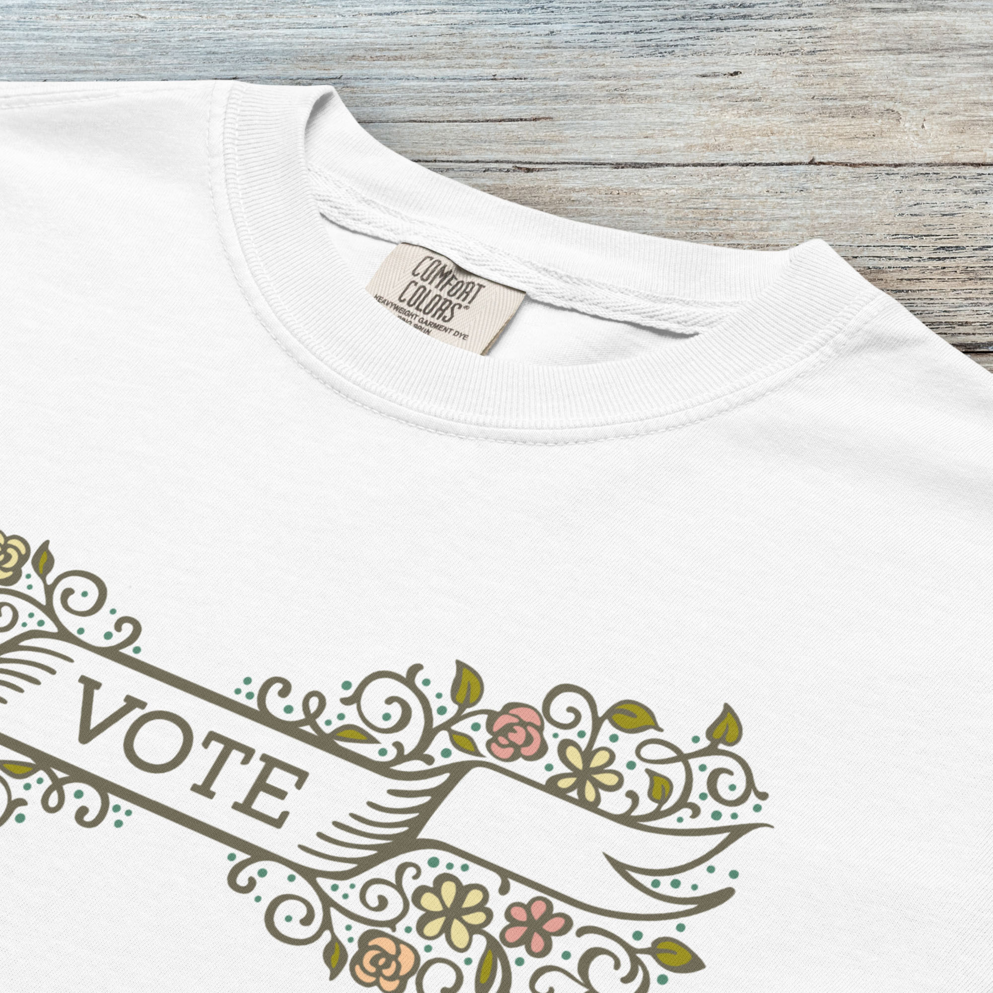 Closeup detail of white t-shirt with vintage style floral illustration and a banner reading “vote” in the center.