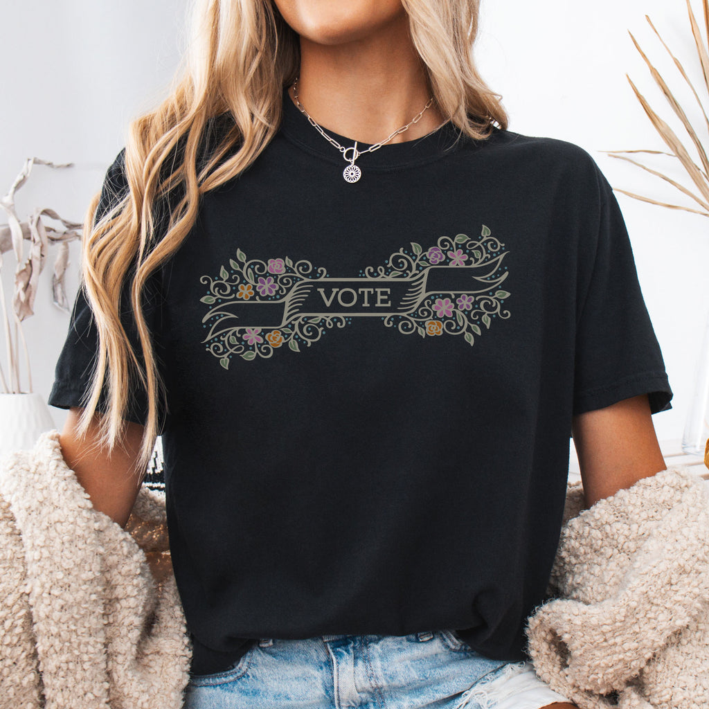 Female model wearing black t-shirt with vintage style floral illustration and a banner reading “vote” in the center.