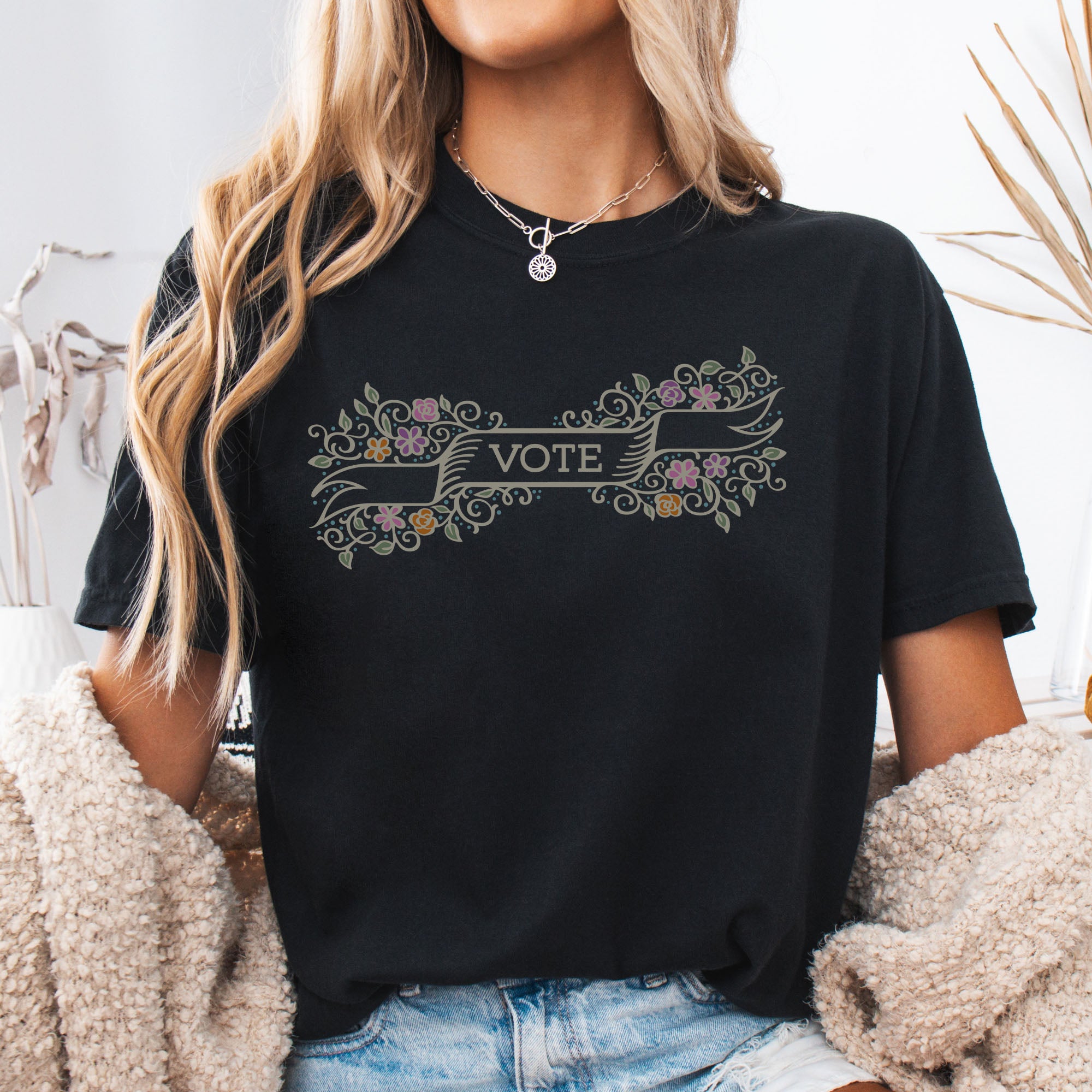Female model wearing black t-shirt with vintage style floral illustration and a banner reading “vote” in the center.
