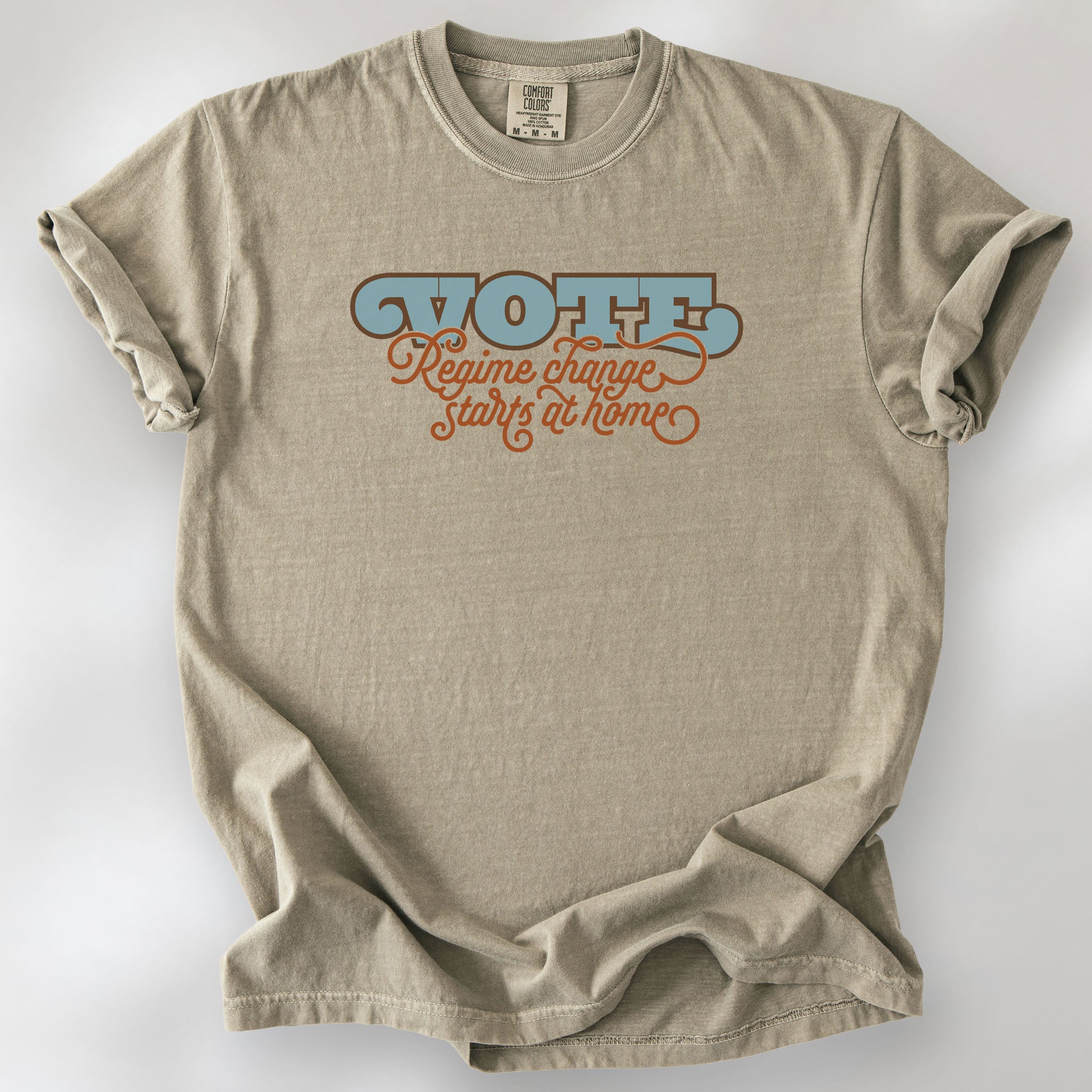 Khaki t-shirt with retro text reading “Vote: Regime Change Starts at Home,” promoting voting and political accountability.