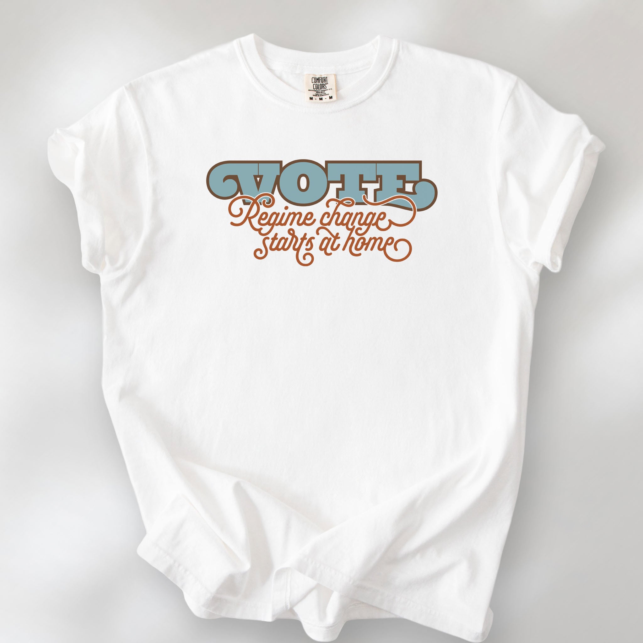 White t-shirt with retro text reading “Vote: Regime Change Starts at Home,” promoting voting and political accountability.