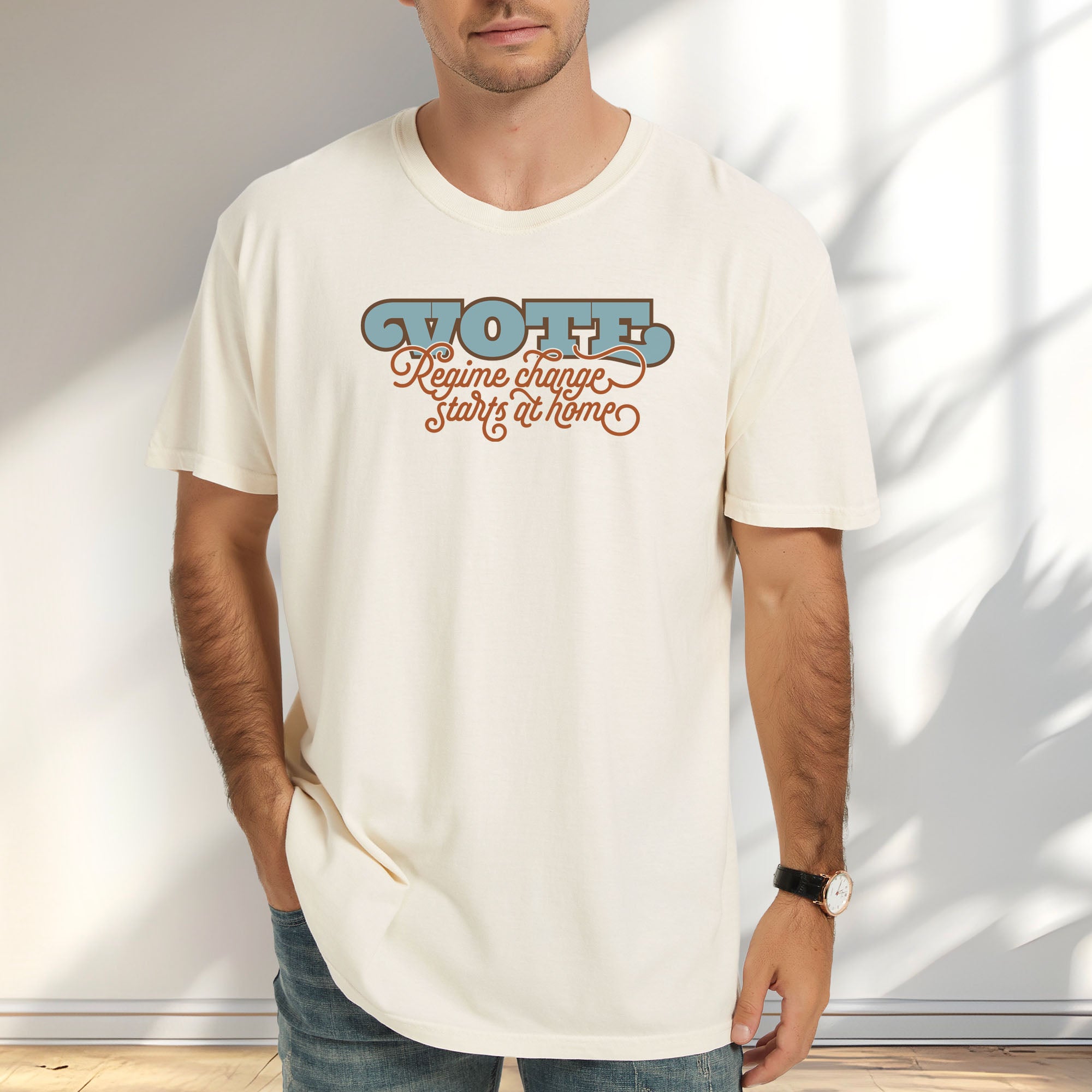 Male model wearing ivory t-shirt with retro text reading “Vote: Regime Change Starts at Home,” promoting voting and political accountability.