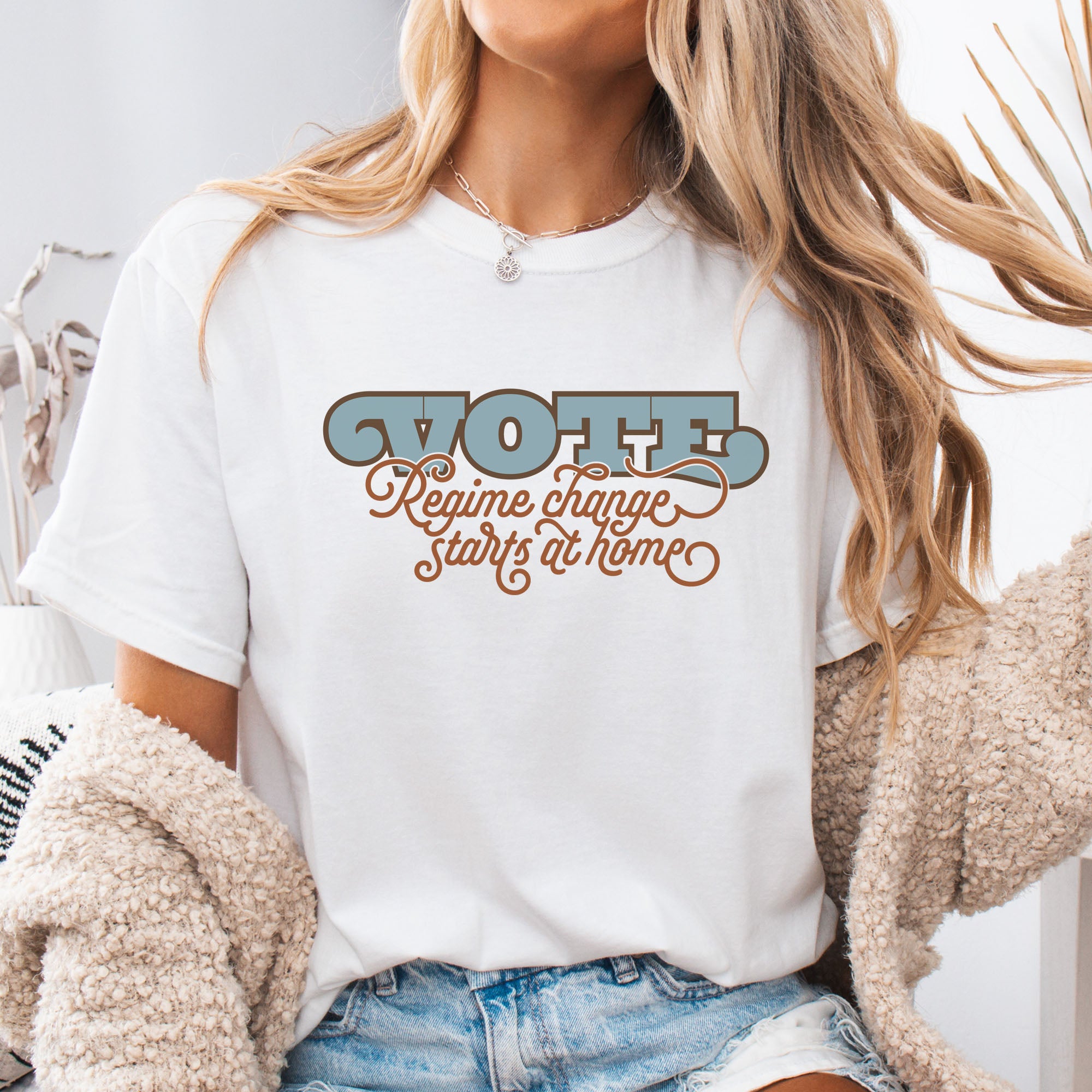 Female model wearing white t-shirt with retro text reading “Vote: Regime Change Starts at Home,” promoting voting and political accountability.