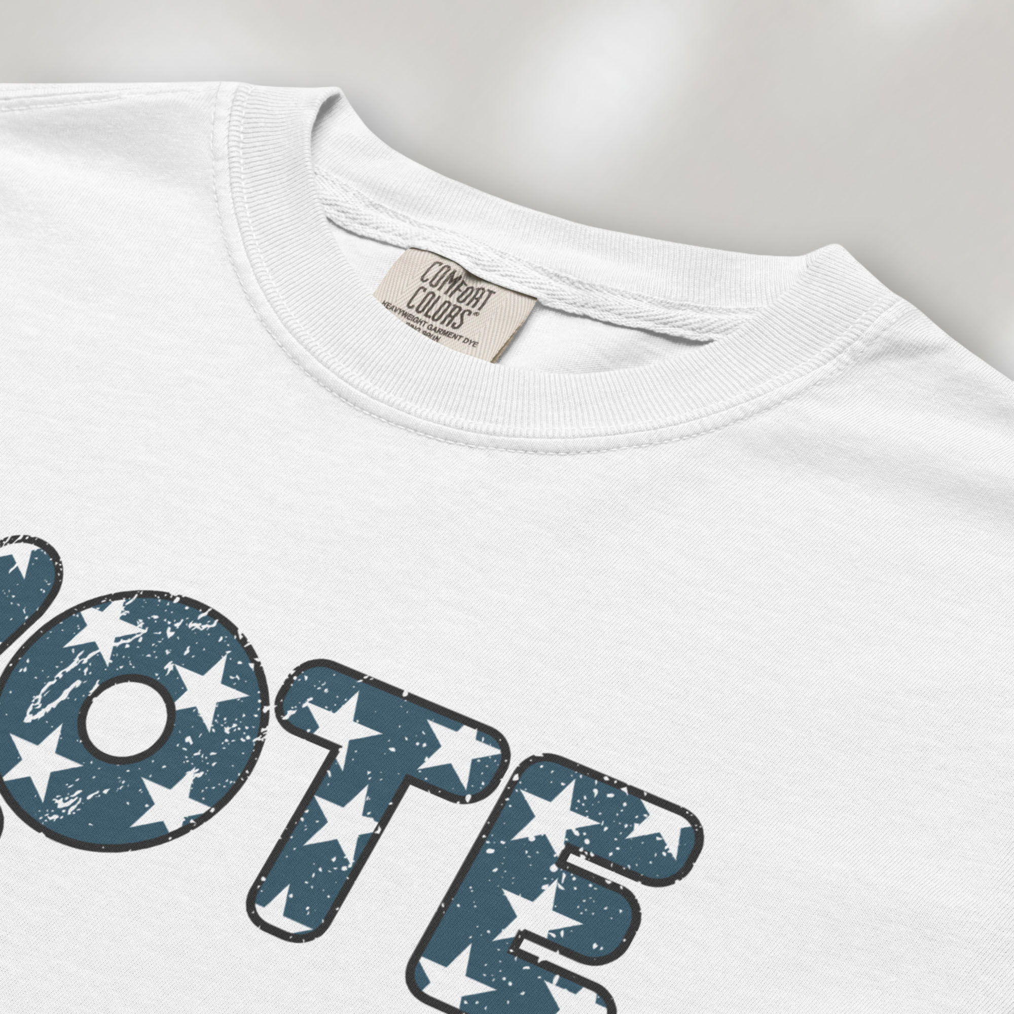 Closeup detail of white t-shirt featuring a distressed retro "VOTE" graphic with blue stars and a vintage red and blue hand making a peace sign.