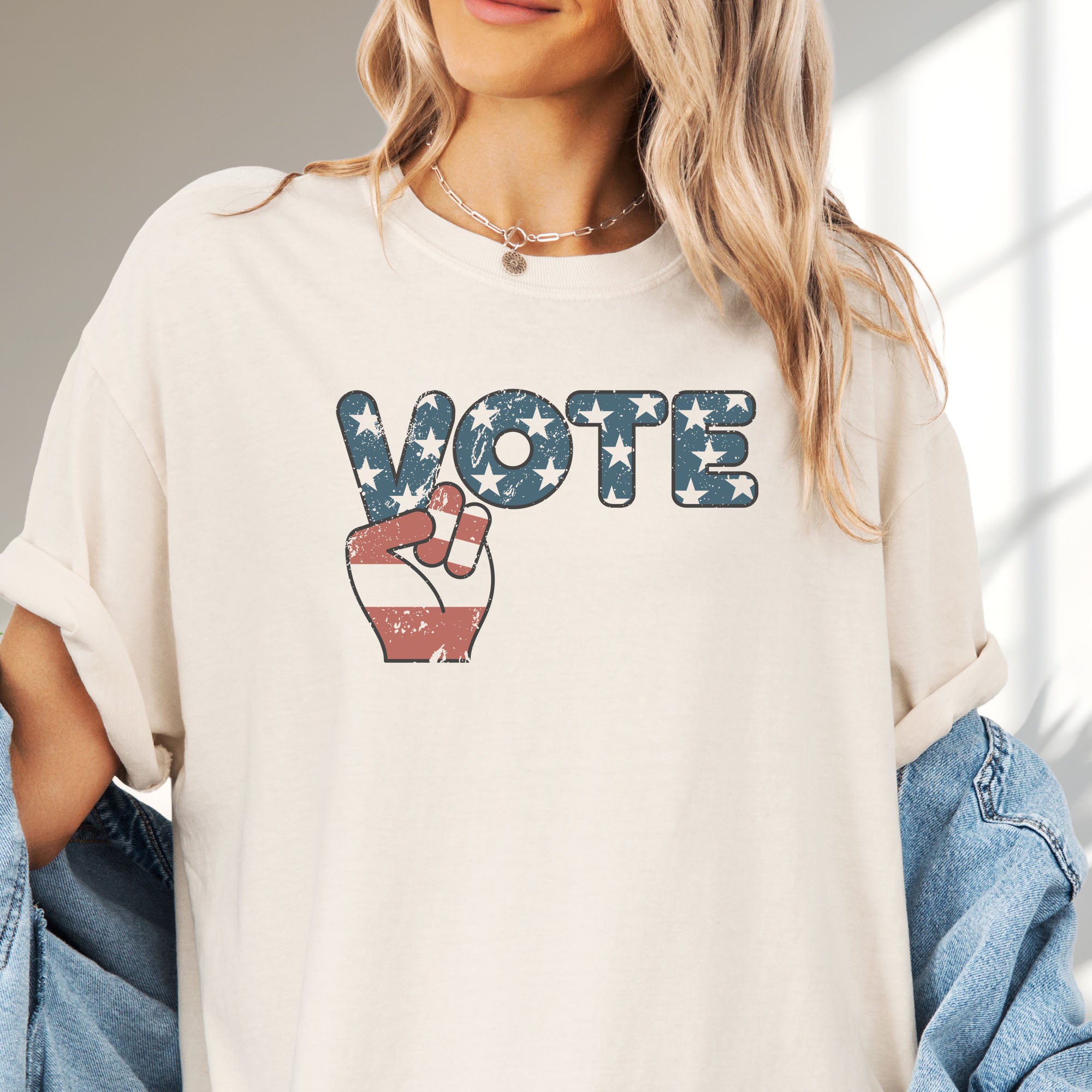 Female model wearing oversized ivory t-shirt featuring a distressed retro "VOTE" graphic with blue stars and a vintage red and blue hand making a peace sign.