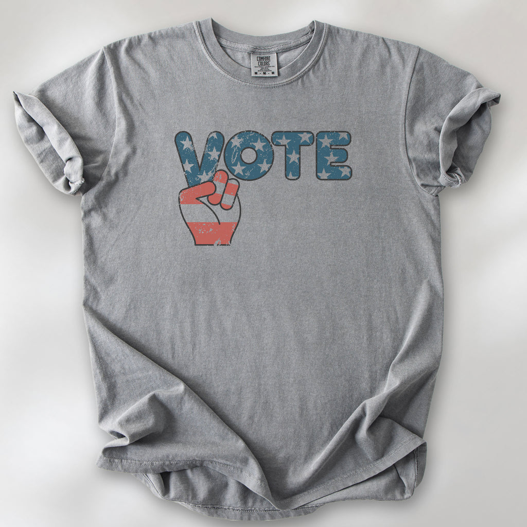 Grey t-shirt featuring a distressed retro "VOTE" graphic with blue stars and a vintage red and blue hand making a peace sign.