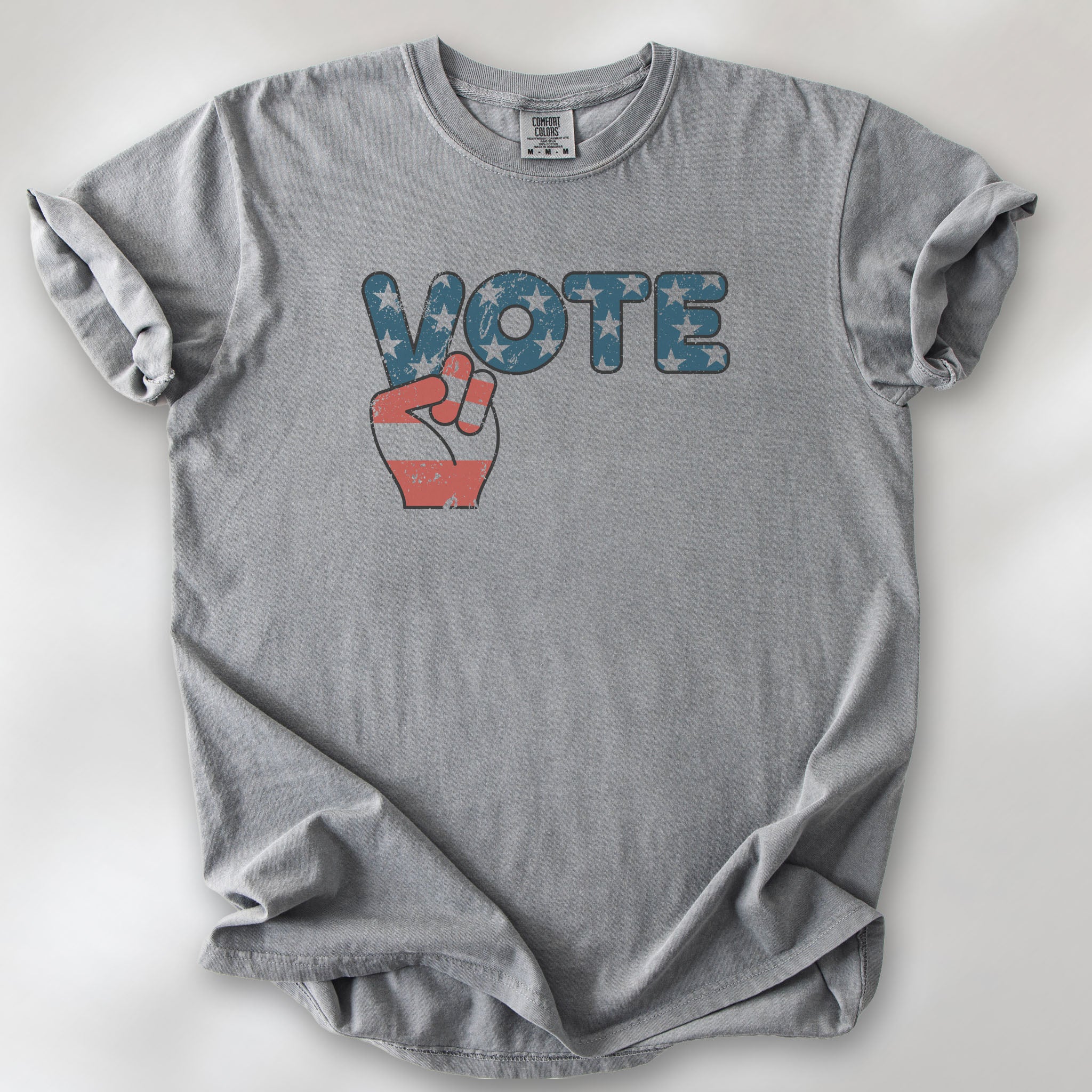 Grey t-shirt featuring a distressed retro "VOTE" graphic with blue stars and a vintage red and blue hand making a peace sign.