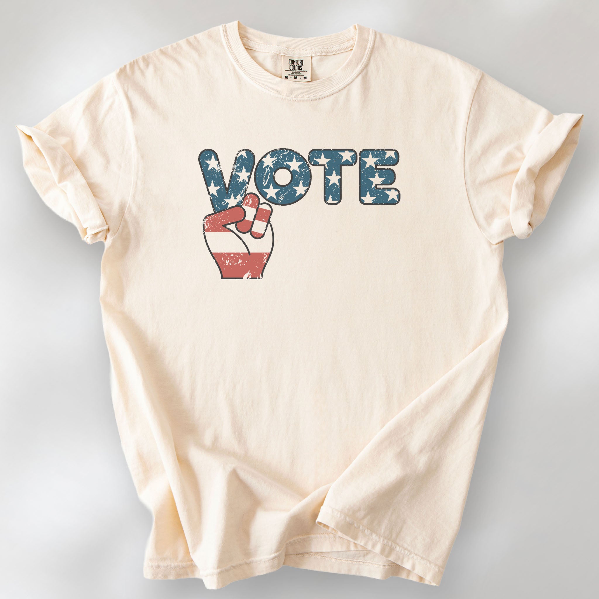 Ivory t-shirt featuring a distressed retro "VOTE" graphic with blue stars and a vintage red and blue hand making a peace sign.