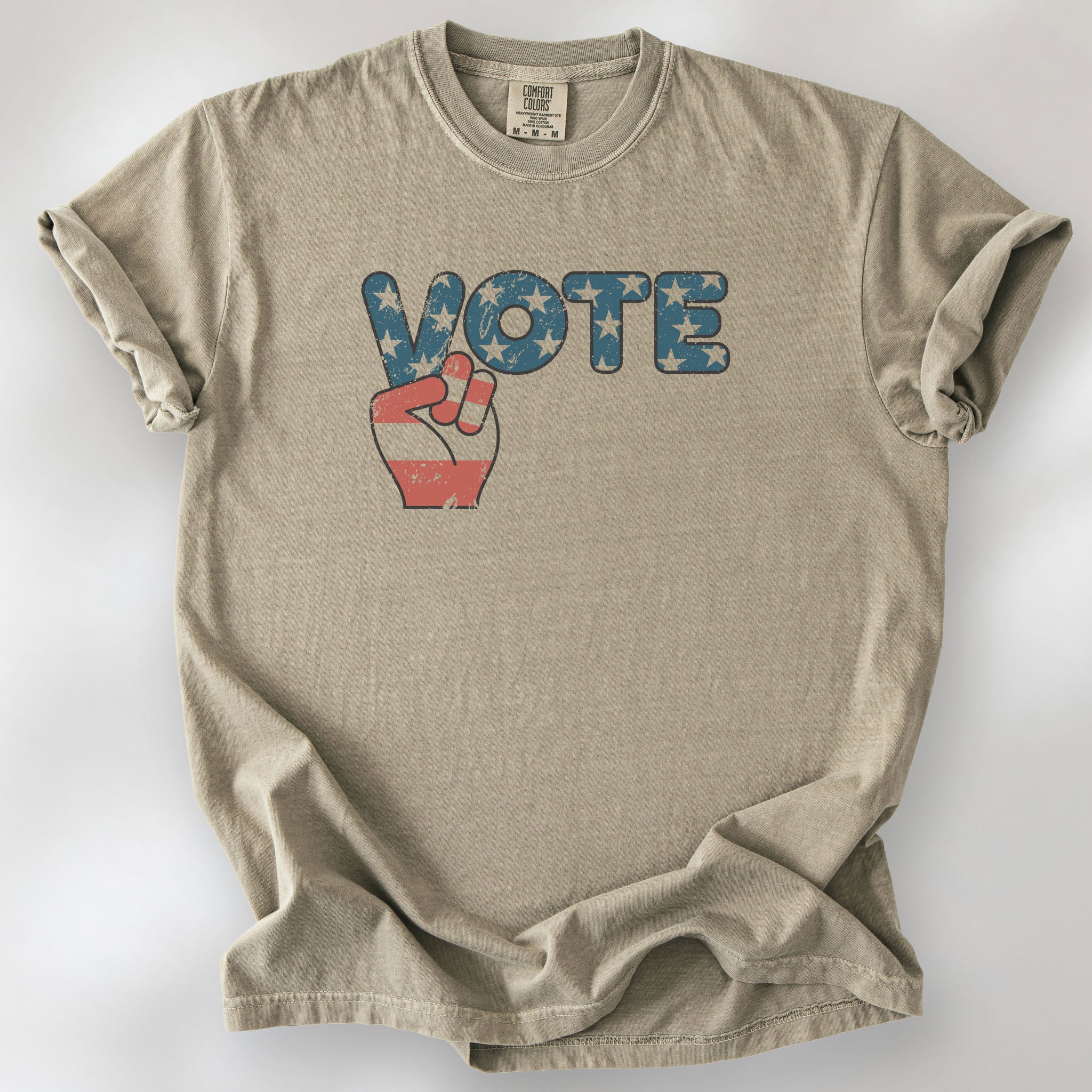 Khaki t-shirt featuring a distressed retro "VOTE" graphic with blue stars and a vintage red and blue hand making a peace sign.