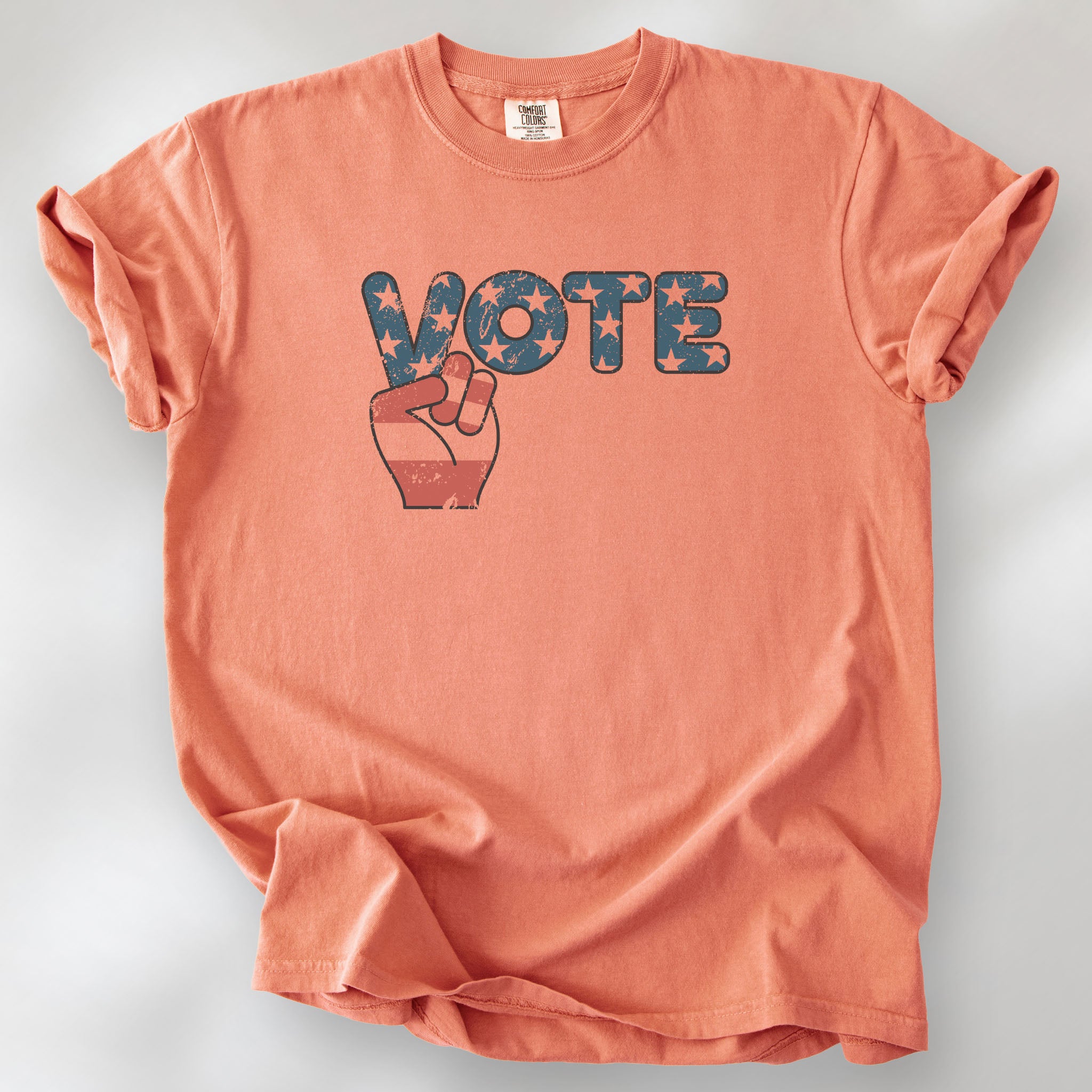 Terracotta t-shirt featuring a distressed retro "VOTE" graphic with blue stars and a vintage red and blue hand making a peace sign.