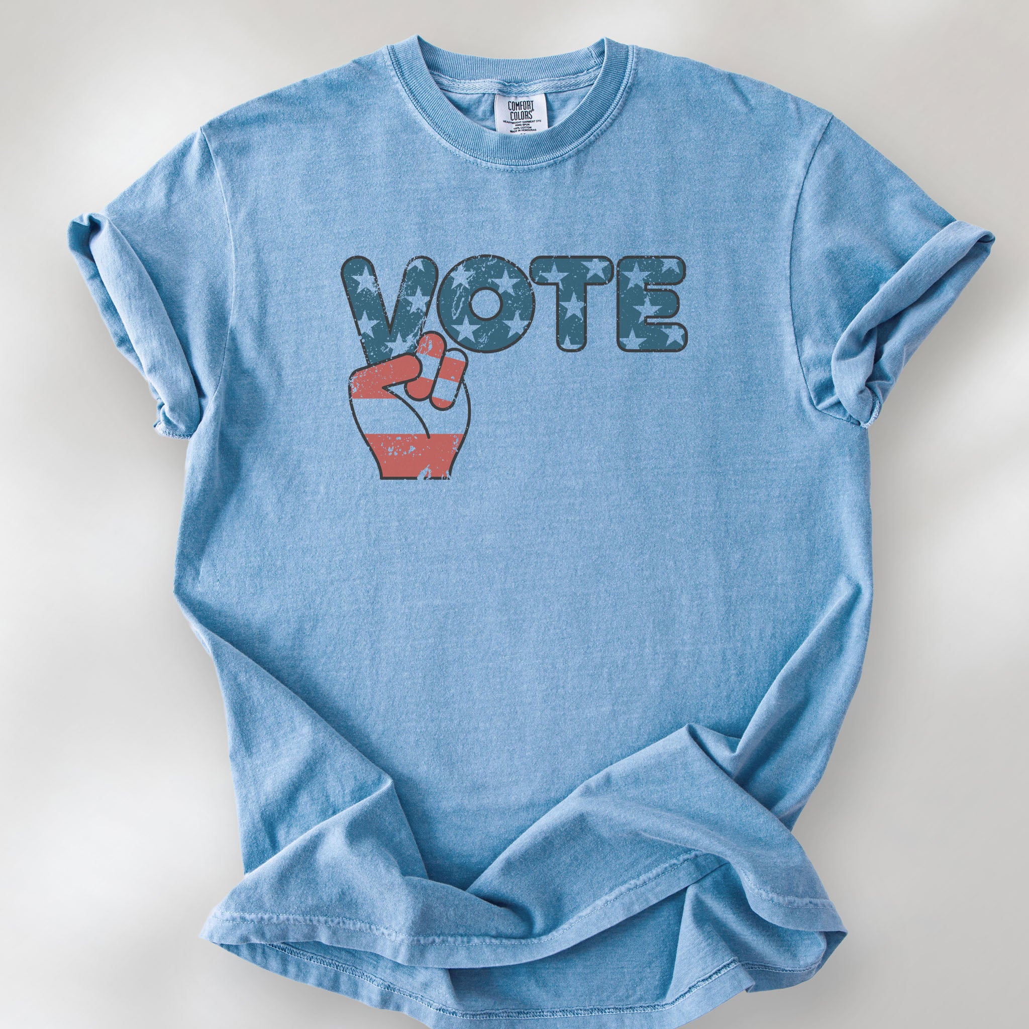 Washed denim t-shirt featuring a distressed retro "VOTE" graphic with blue stars and a vintage red and blue hand making a peace sign.