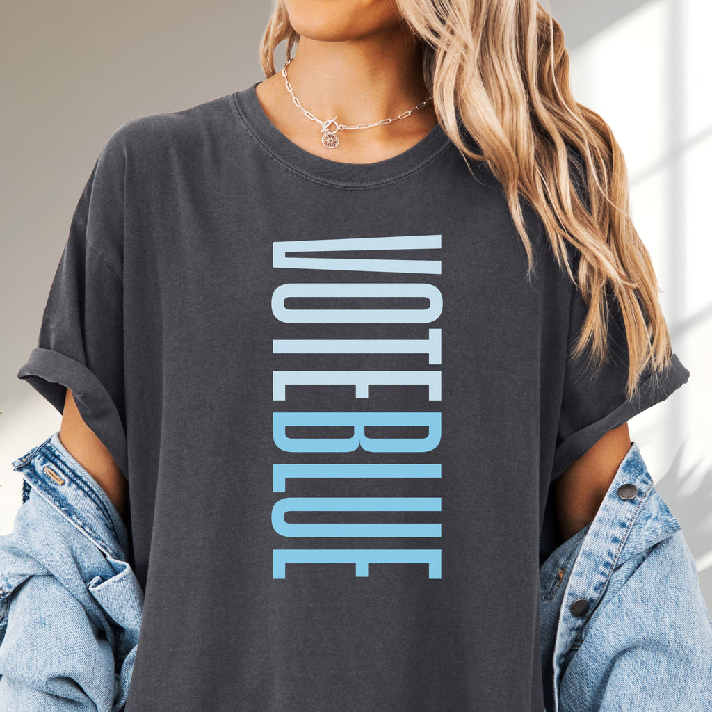 Female model wearing pepper t-shirt featuring the words "VOTE BLUE" stacked vertically in bold minimalist blue typography.