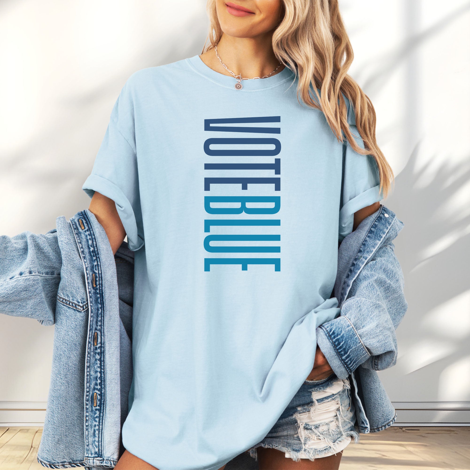 Female model wearing oversized chambray t-shirt featuring the words "VOTE BLUE" stacked vertically in bold minimalist blue typography.