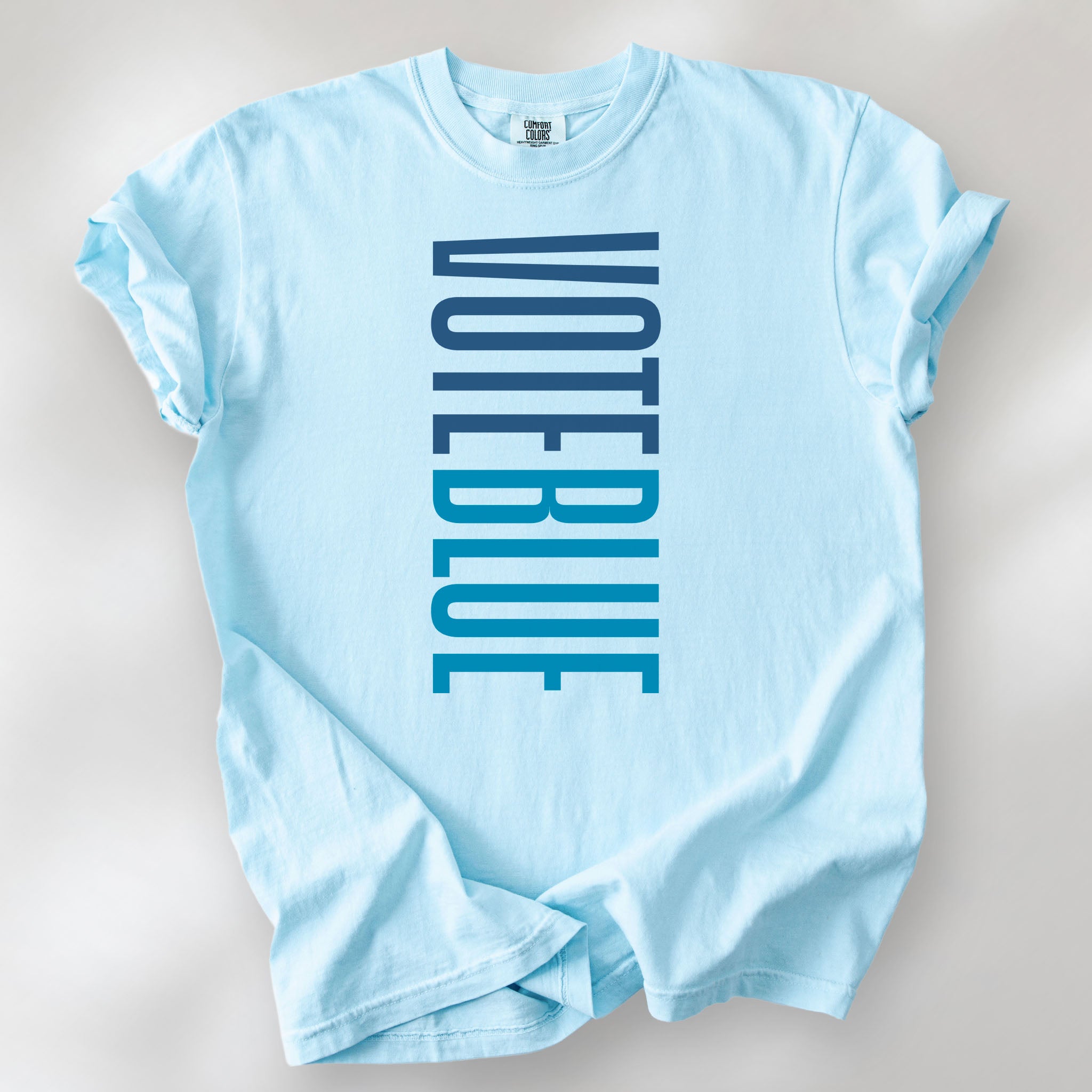 Chambray t-shirt featuring the words "VOTE BLUE" stacked vertically in bold minimalist blue typography.