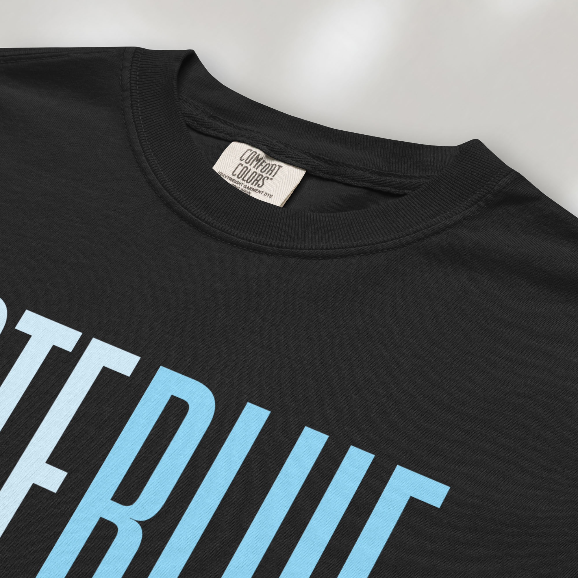 Closeup detail of black t-shirt featuring the words "VOTE BLUE" in bold horizontal blue geometric typography with a clean minimalist design.