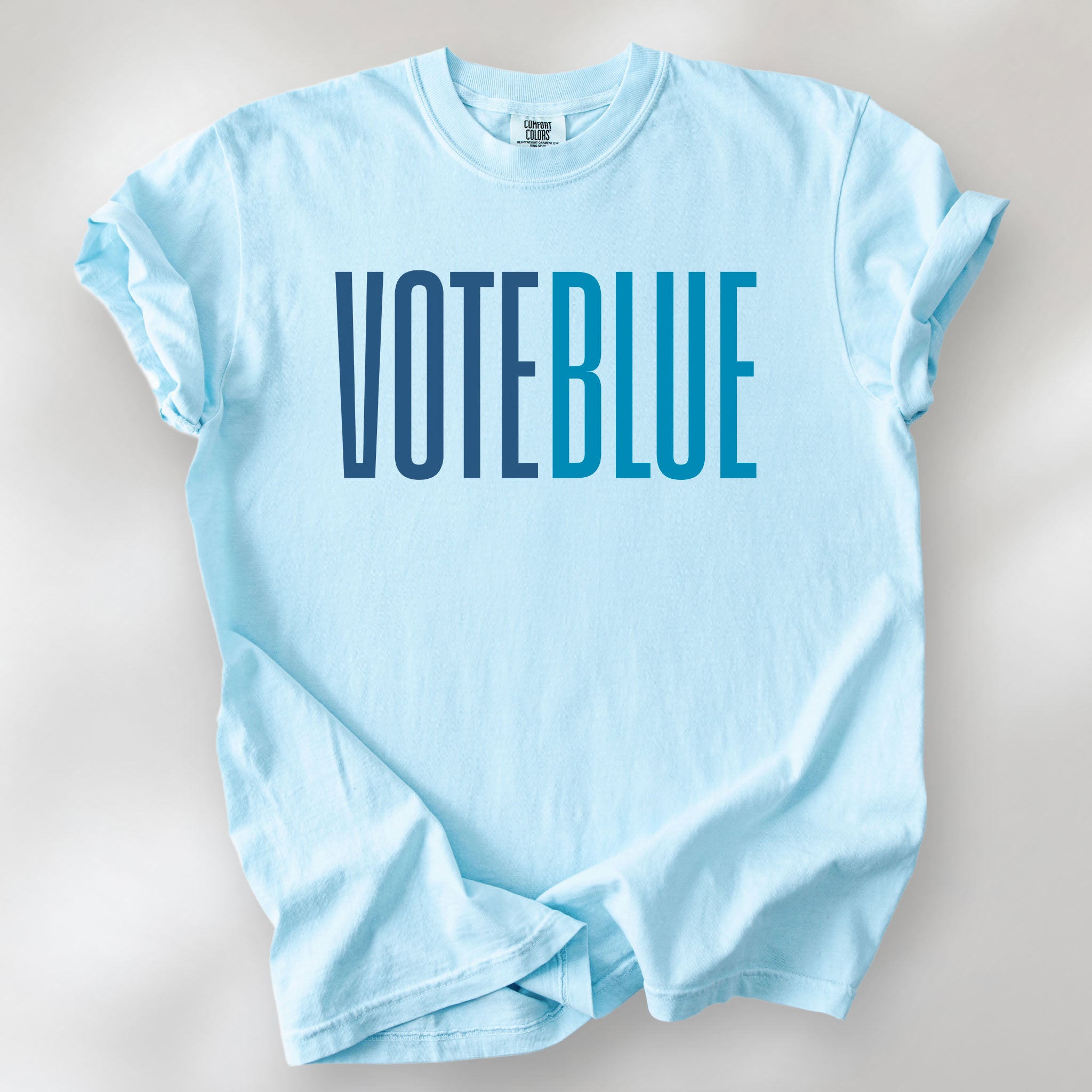 Chambray t-shirt featuring the words "VOTE BLUE" in bold horizontal blue geometric typography with a clean minimalist design.