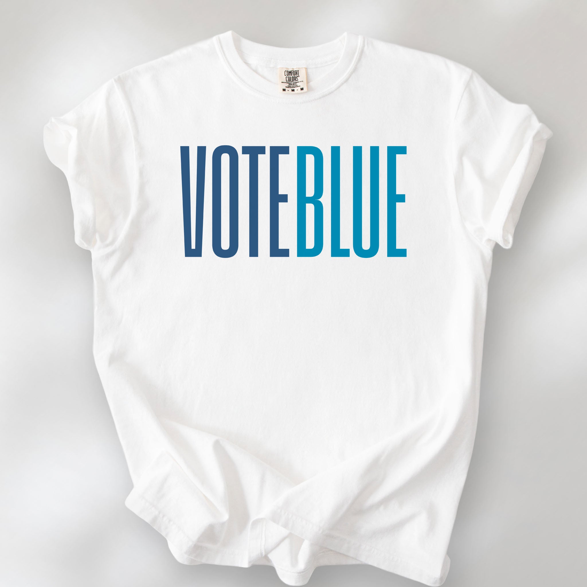 White t-shirt featuring the words "VOTE BLUE" in bold horizontal blue geometric typography with a clean minimalist design.