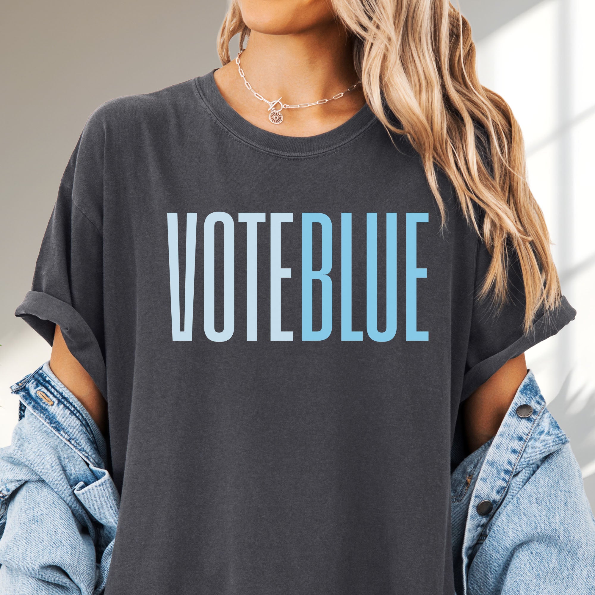 Female model wearing pepper t-shirt featuring the words "VOTE BLUE" in bold horizontal blue geometric typography with a clean minimalist design.
