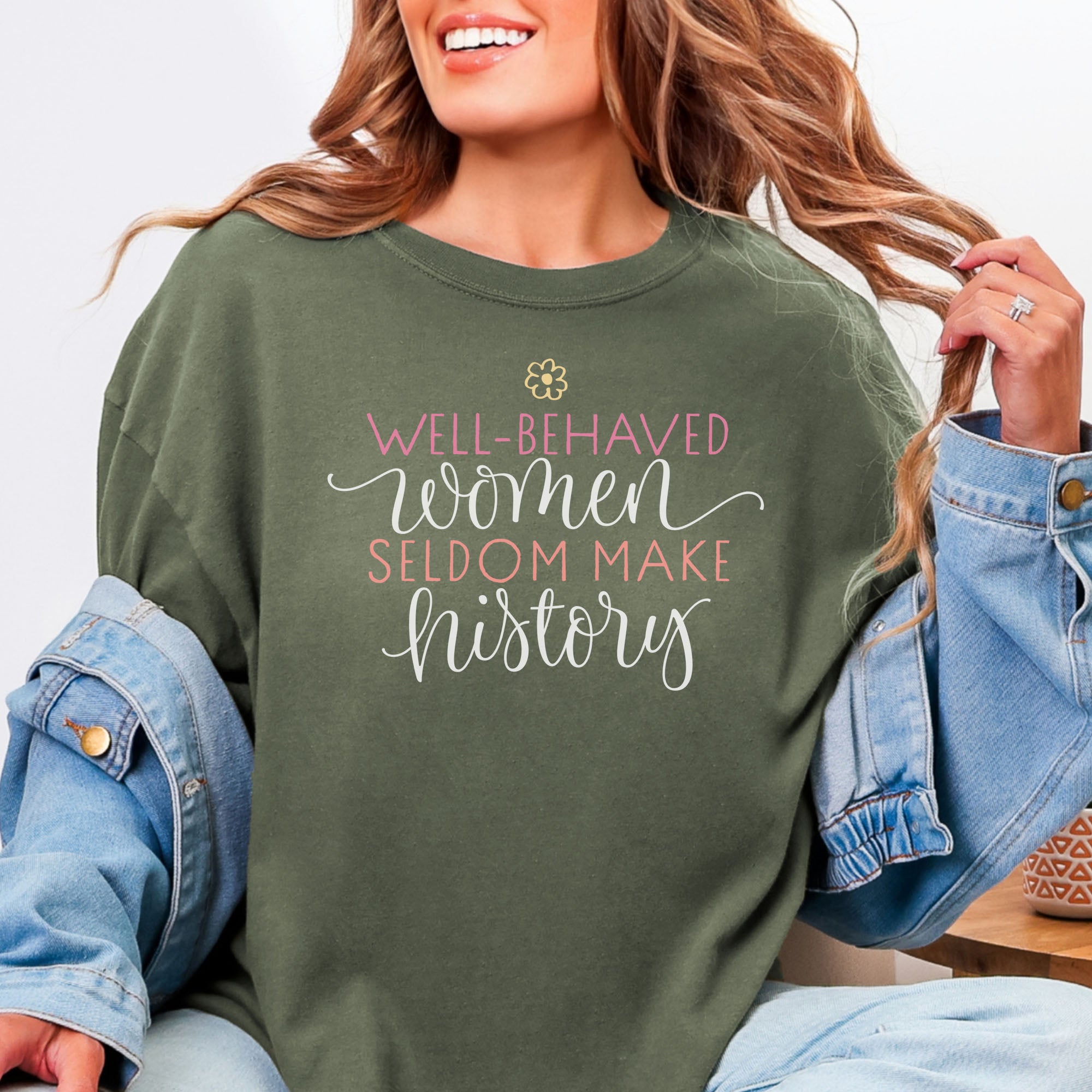 Female model wearing sage feminist t-shirt with colorful text that reads “Well-behaved women seldom make history” — empowering women’s rights shirt and activist apparel.