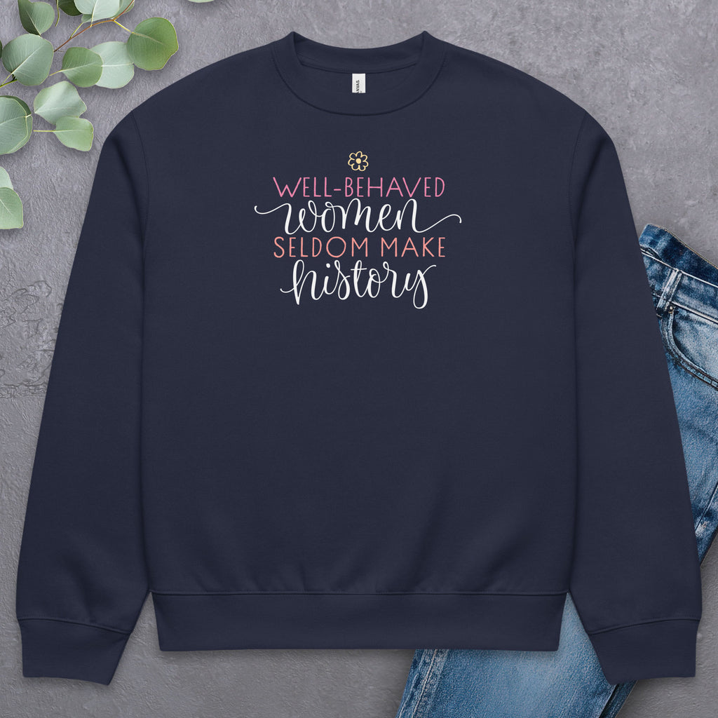 Navy crewneck sweatshirt with stylized text graphic that reads "well-behaved women seldom make history",  laying flat with a pair of jeans.