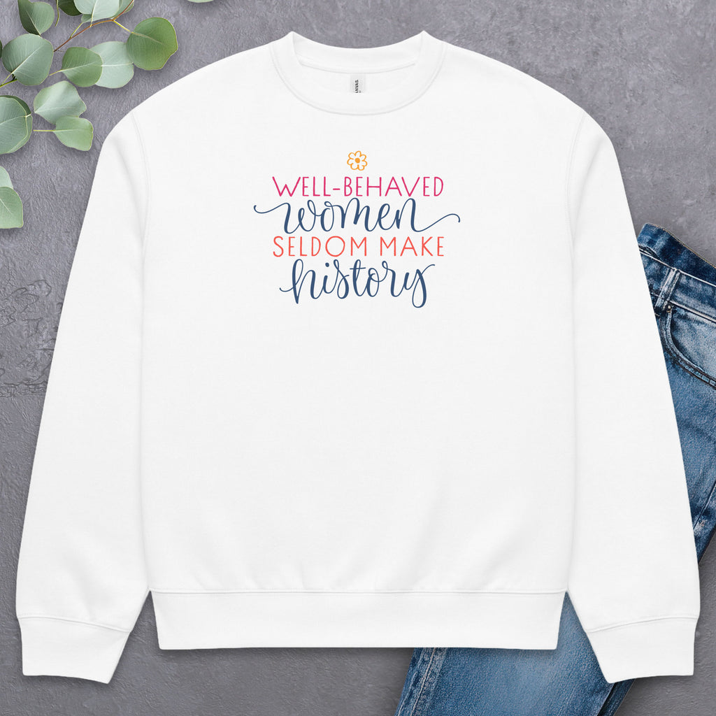 White crewneck sweatshirt with stylized text graphic that reads "well-behaved women seldom make history",  laying flat with a pair of jeans.