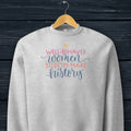 Athletic heather grey crewneck sweatshirt with stylized text graphic that reads "well-behaved women seldom make history" hanging on a hanger.