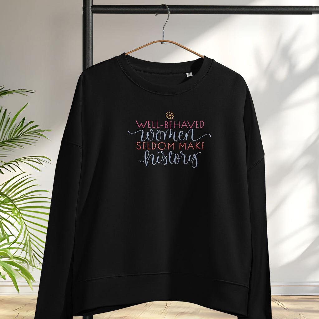 Black crewneck sweatshirt with stylized text graphic that reads "well-behaved women seldom make history" hanging on a hanger.