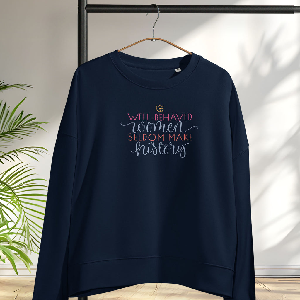 Navy crewneck sweatshirt with stylized text graphic that reads "well-behaved women seldom make history" hanging on a hanger.