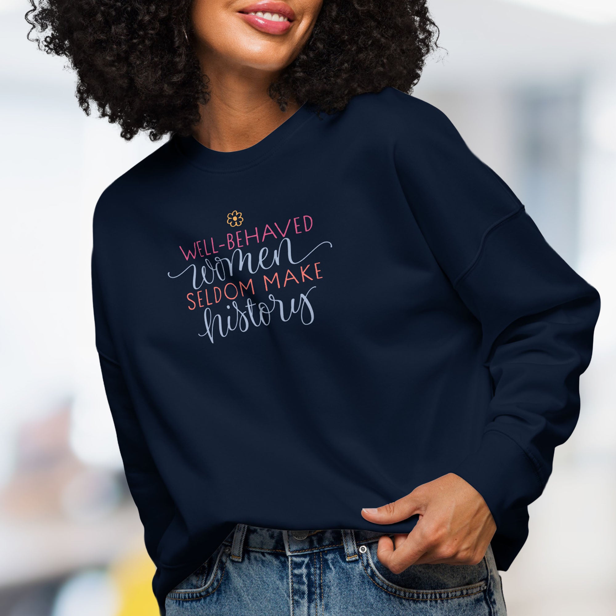 Front view of female model wearing navy crewneck sweatshirt with stylized text graphic that reads "well-behaved women seldom make history".