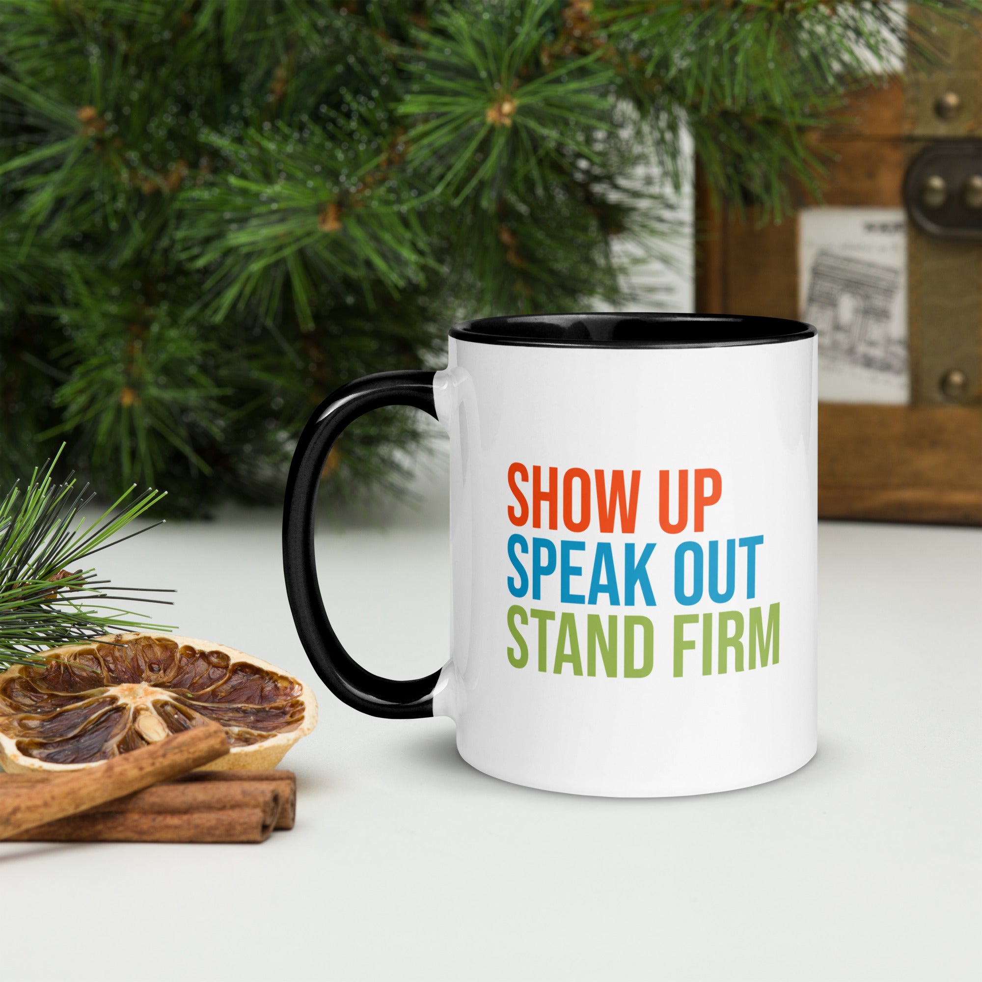 Coffee mug with black handle and inside with text on one side that reads "show up, speak out, stand firm." The other side, not shown in photo, reads "democracy doesn't defend itself."
