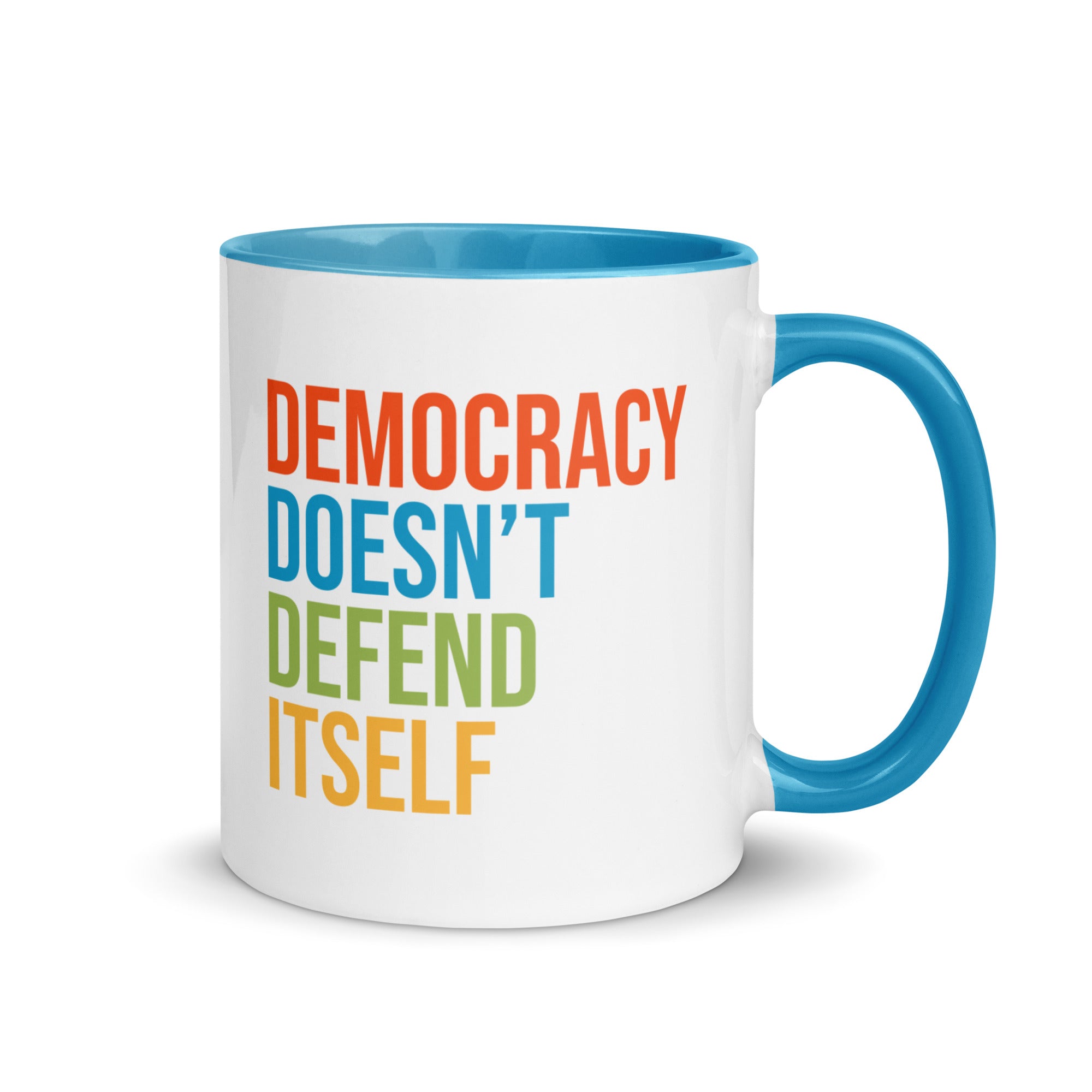 Coffee mug with bright blue handle and inside with text on one side that reads "democracy doesn't defend itself." The other side, not shown in photo, reads "show up, speak out, stand firm."