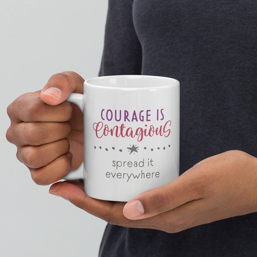 Person holding mug with styled text graphic that reads "courage is contagious – spread it everywhere", with handle on left.