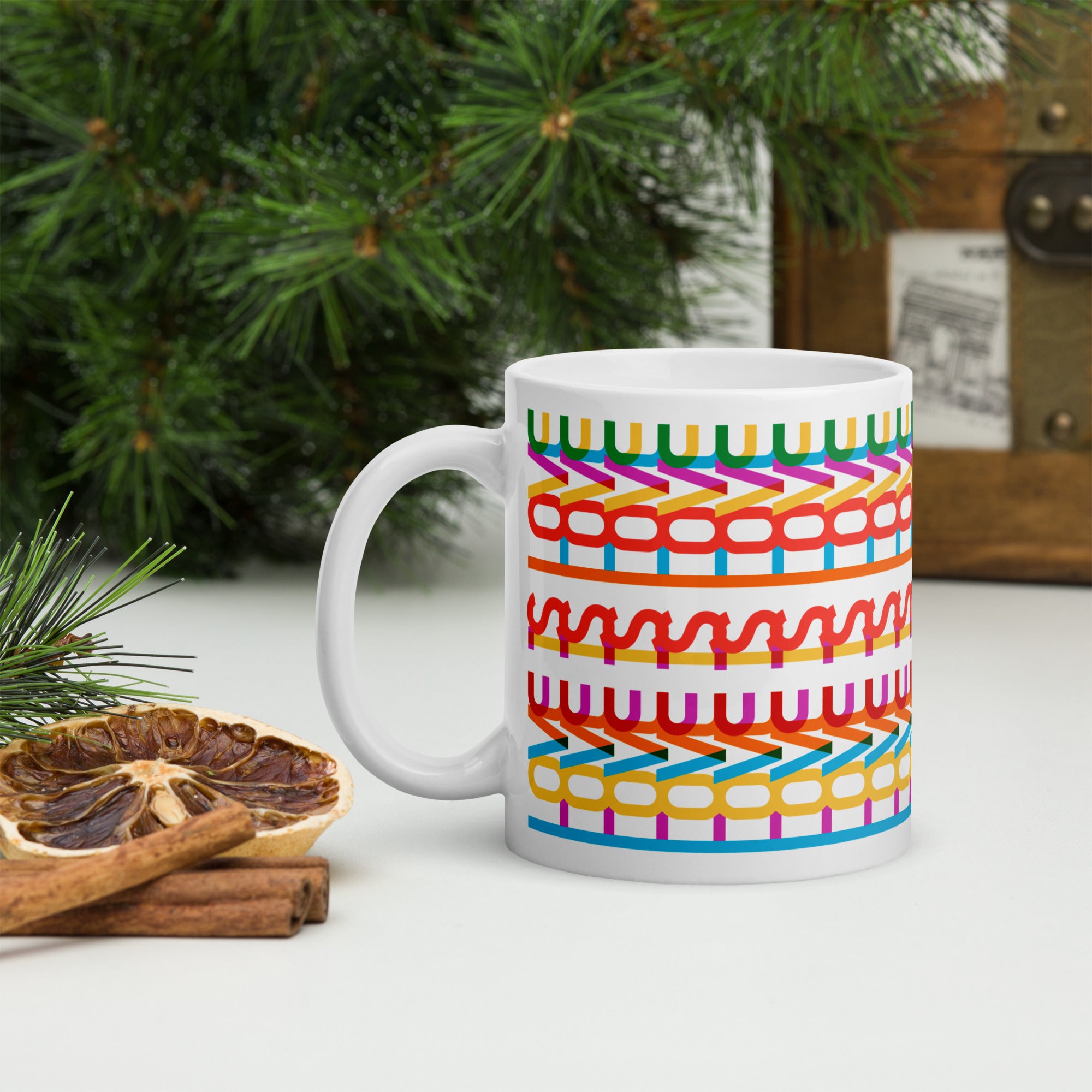 Colorful coffee mug with a repeating hidden “love is love” message in the Gilbert font, featuring bright rainbow-inspired patterns wrapped around the mug, on a tabletop with forest greenery.