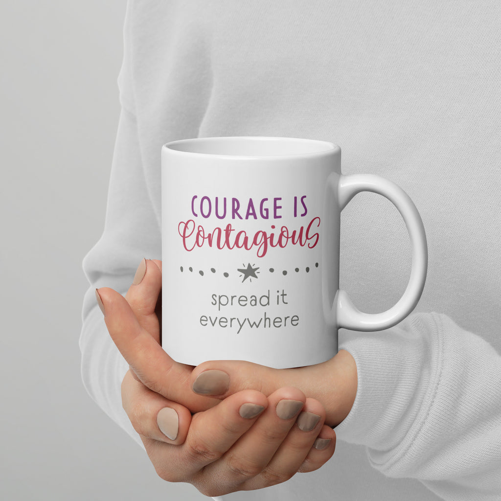 Person holding mug with styled text graphic that reads "courage is contagious – spread it everywhere", with handle on right.