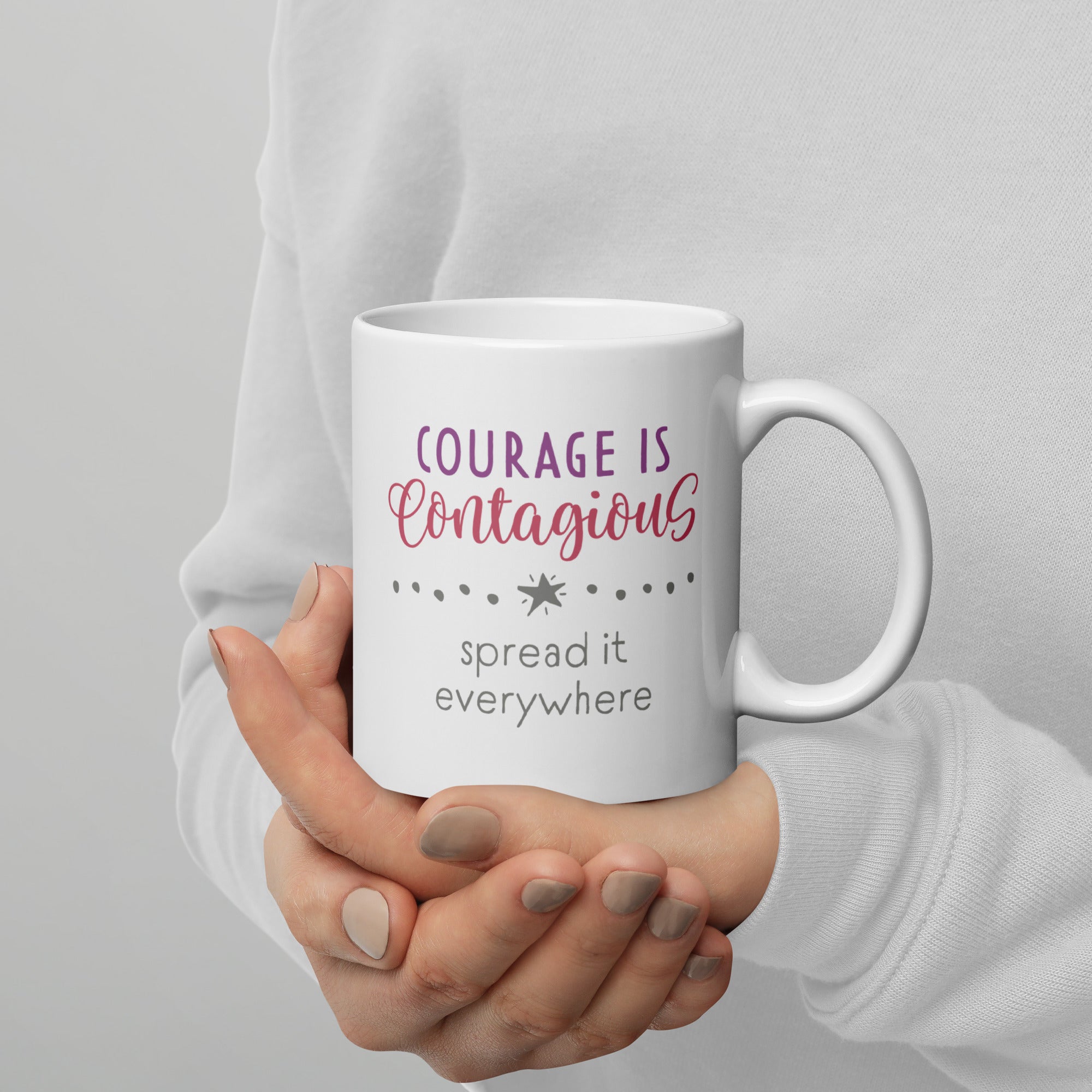 Person holding mug with styled text graphic that reads "courage is contagious – spread it everywhere", with handle on right.