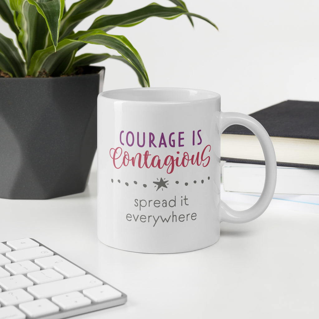 Mug with styled text graphic that reads "courage is contagious – spread it everywhere", on a desk with plant and keyboard.