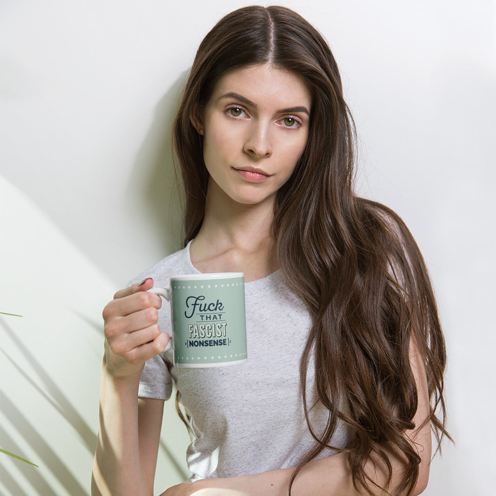 Person holding mug with graphic on mint green background and navy styled text block that reads "fuck that fascist nonsense." 