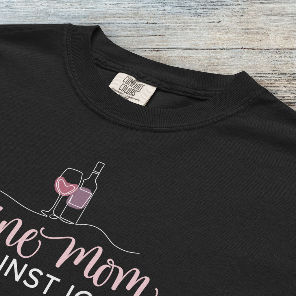 Closeup details of black t-shirt featuring the text “Wine Mom Against ICE” with a minimalist illustration of a wine bottle and glass above the lettering.