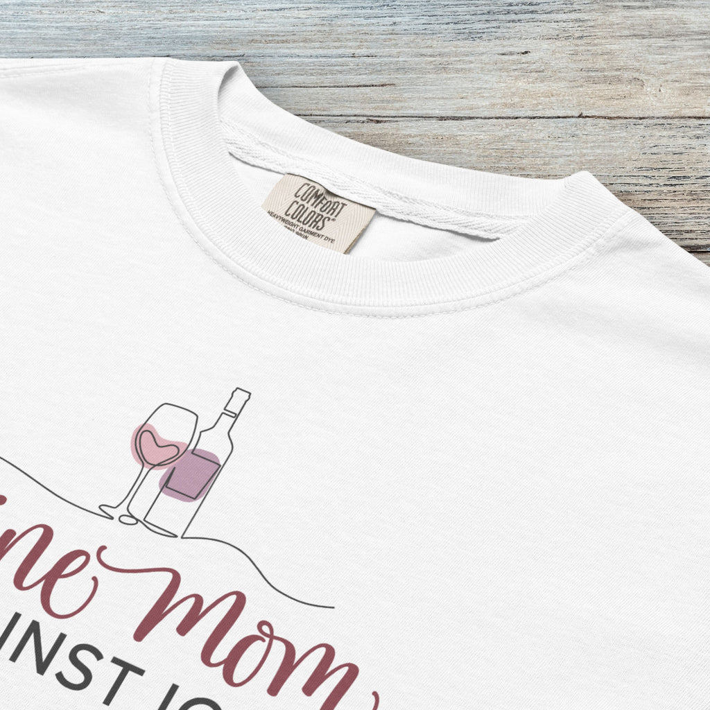 Closeup detail of white t-shirt featuring the text “Wine Mom Against ICE” with a minimalist illustration of a wine bottle and glass above the lettering.
