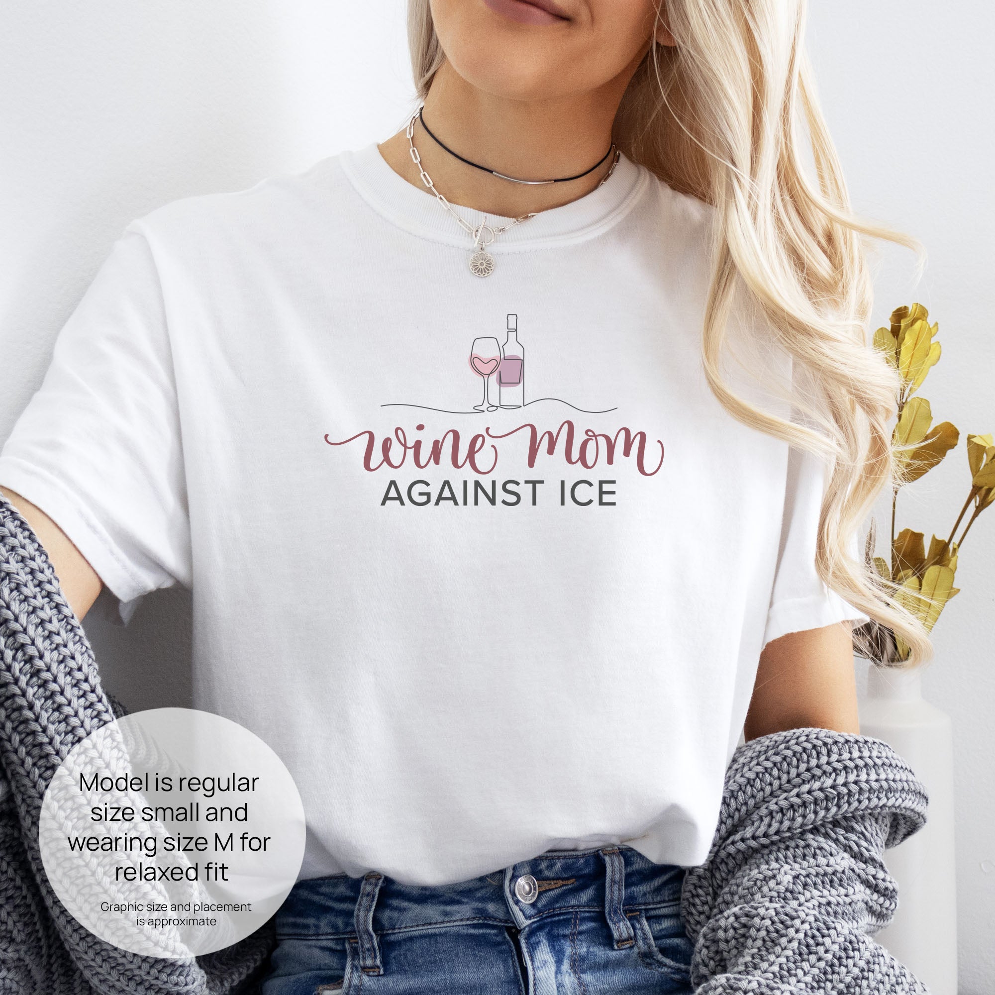 Female model wearing white t-shirt featuring the text “Wine Mom Against ICE” with a minimalist illustration of a wine bottle and glass above the lettering. Includes size and fit information for the model who is regular size small, and wearing a size M shirt for a relaxed fit.
