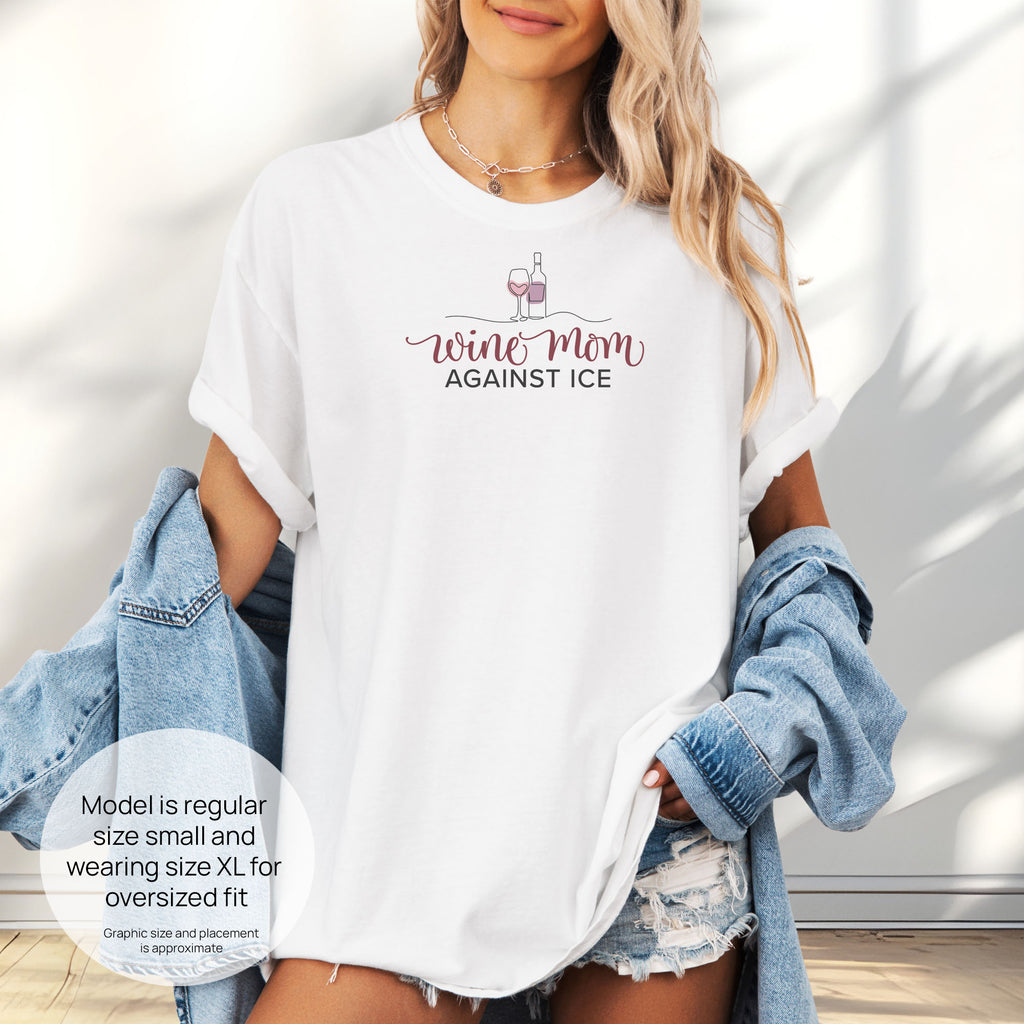 Female model wearing white t-shirt featuring the text “Wine Mom Against ICE” with a minimalist illustration of a wine bottle and glass above the lettering. Includes size and fit information for the model who is regular size small, and wearing a size XL shirt for an oversized fit.
