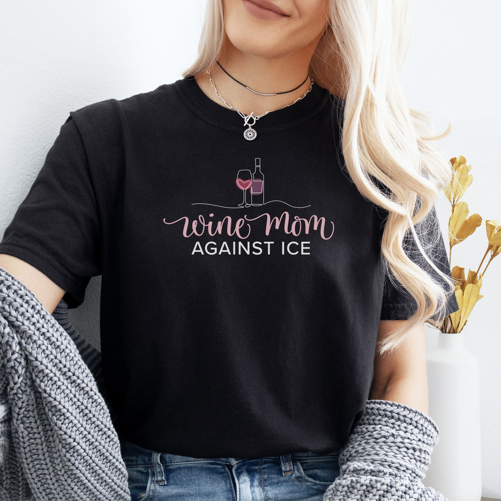 Female model wearing black t-shirt featuring the text “Wine Mom Against ICE” with a minimalist illustration of a wine bottle and glass above the lettering.