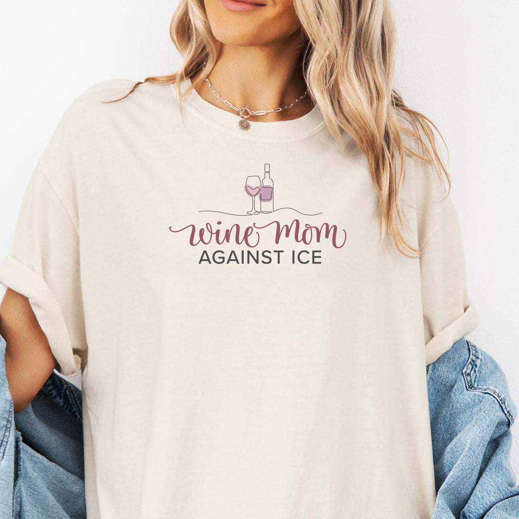 Female model wearing oversized ivory t-shirt featuring the text “Wine Mom Against ICE” with a minimalist illustration of a wine bottle and glass above the lettering.