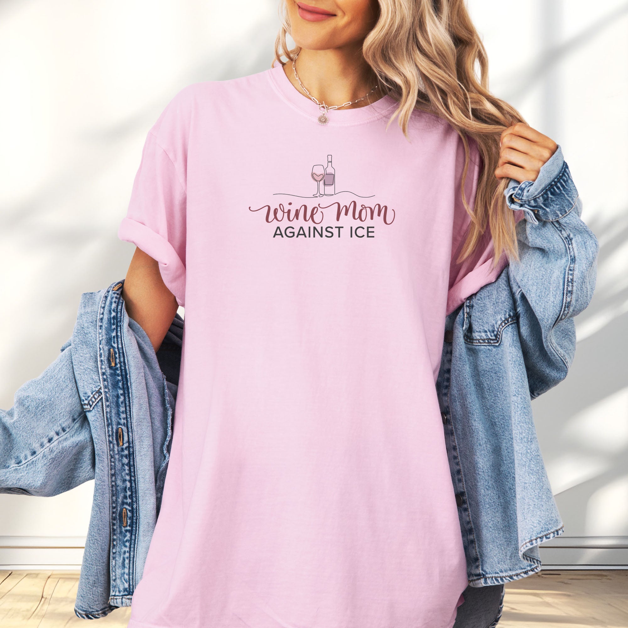 Female model wearing blossom t-shirt featuring the text “Wine Mom Against ICE” with a minimalist illustration of a wine bottle and glass above the lettering.