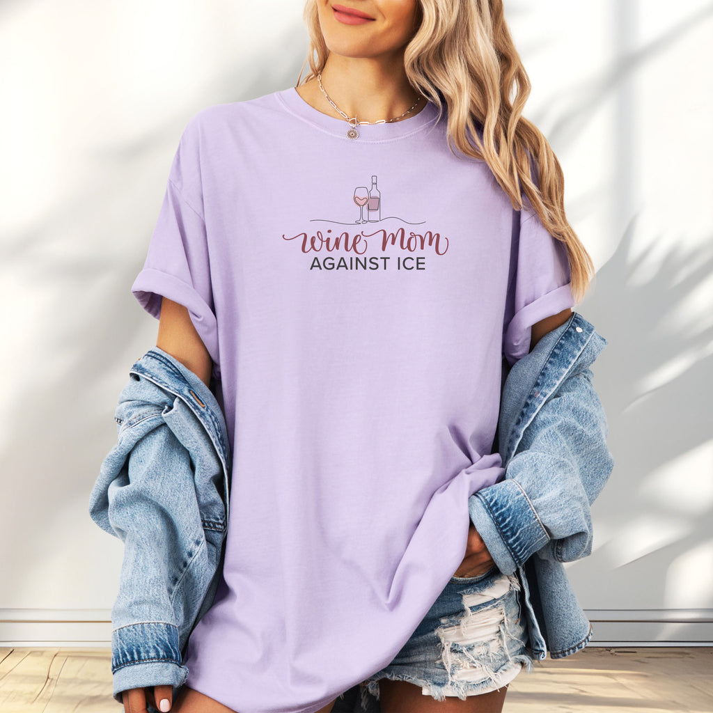 Female model wearing oversized orchid t-shirt featuring the text “Wine Mom Against ICE” with a minimalist illustration of a wine bottle and glass above the lettering.