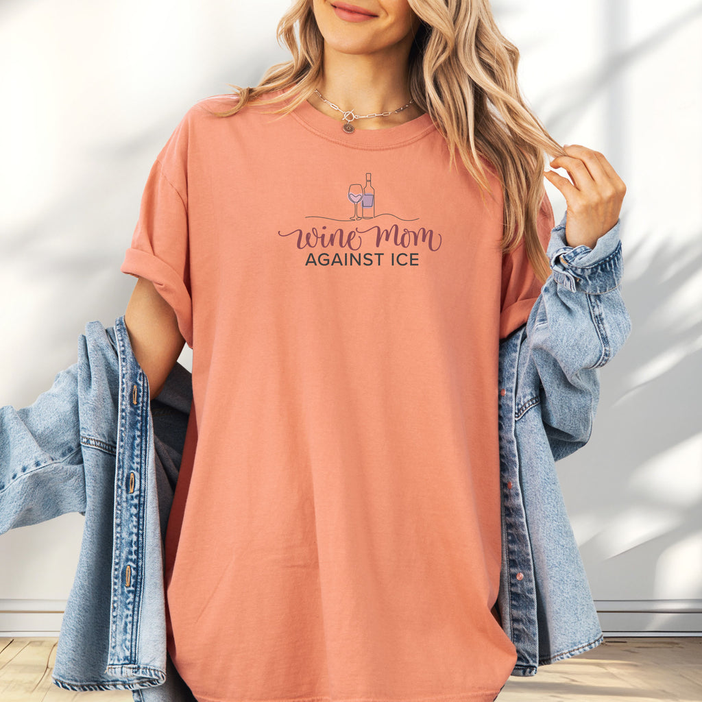 Female model wearing terracotta t-shirt featuring the text “Wine Mom Against ICE” with a minimalist illustration of a wine bottle and glass above the lettering.