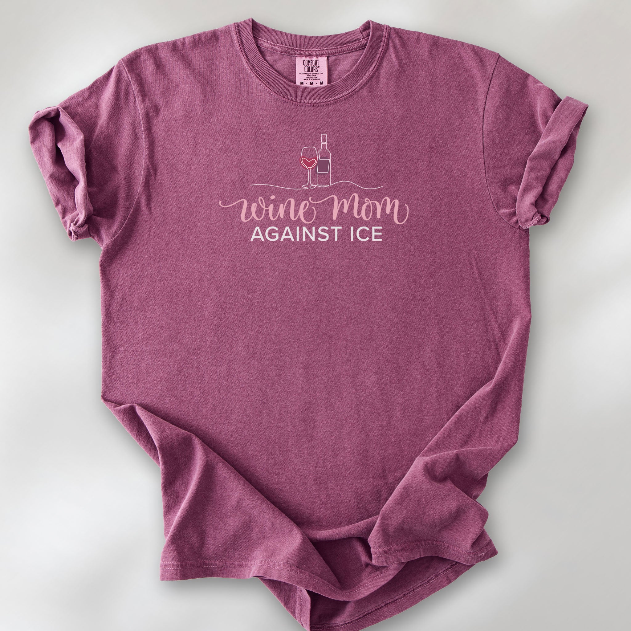 Berry t-shirt featuring the text “Wine Mom Against ICE” with a minimalist illustration of a wine bottle and glass above the lettering.