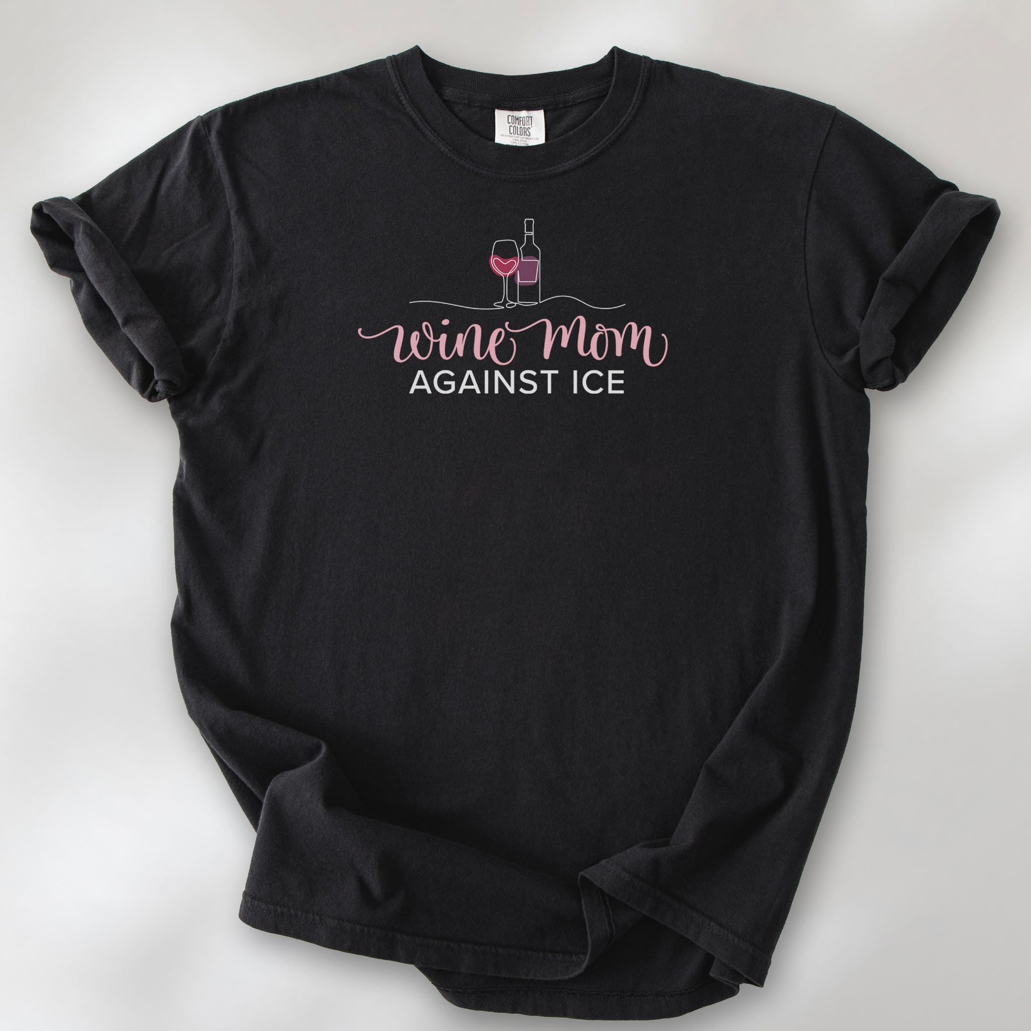 Black t-shirt featuring the text “Wine Mom Against ICE” with a minimalist illustration of a wine bottle and glass above the lettering.
