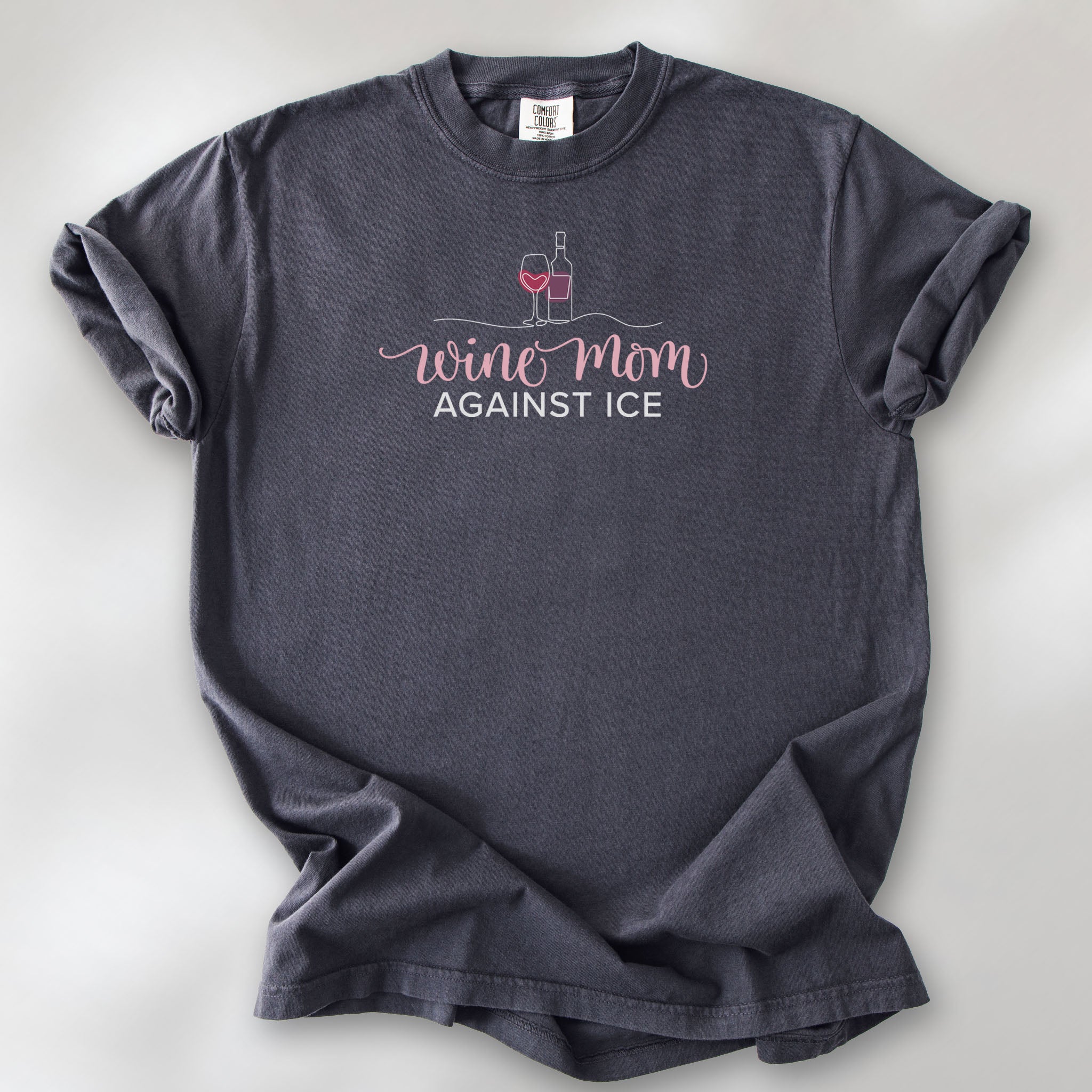 Graphite t-shirt featuring the text “Wine Mom Against ICE” with a minimalist illustration of a wine bottle and glass above the lettering.