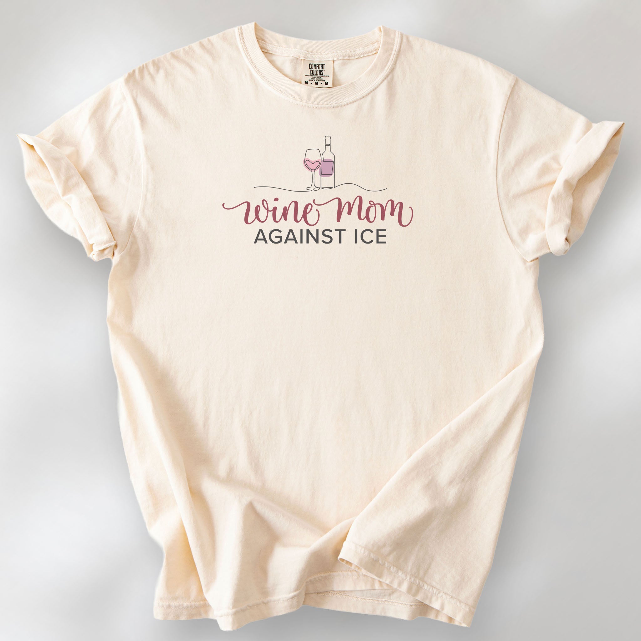 Ivory t-shirt featuring the text “Wine Mom Against ICE” with a minimalist illustration of a wine bottle and glass above the lettering.